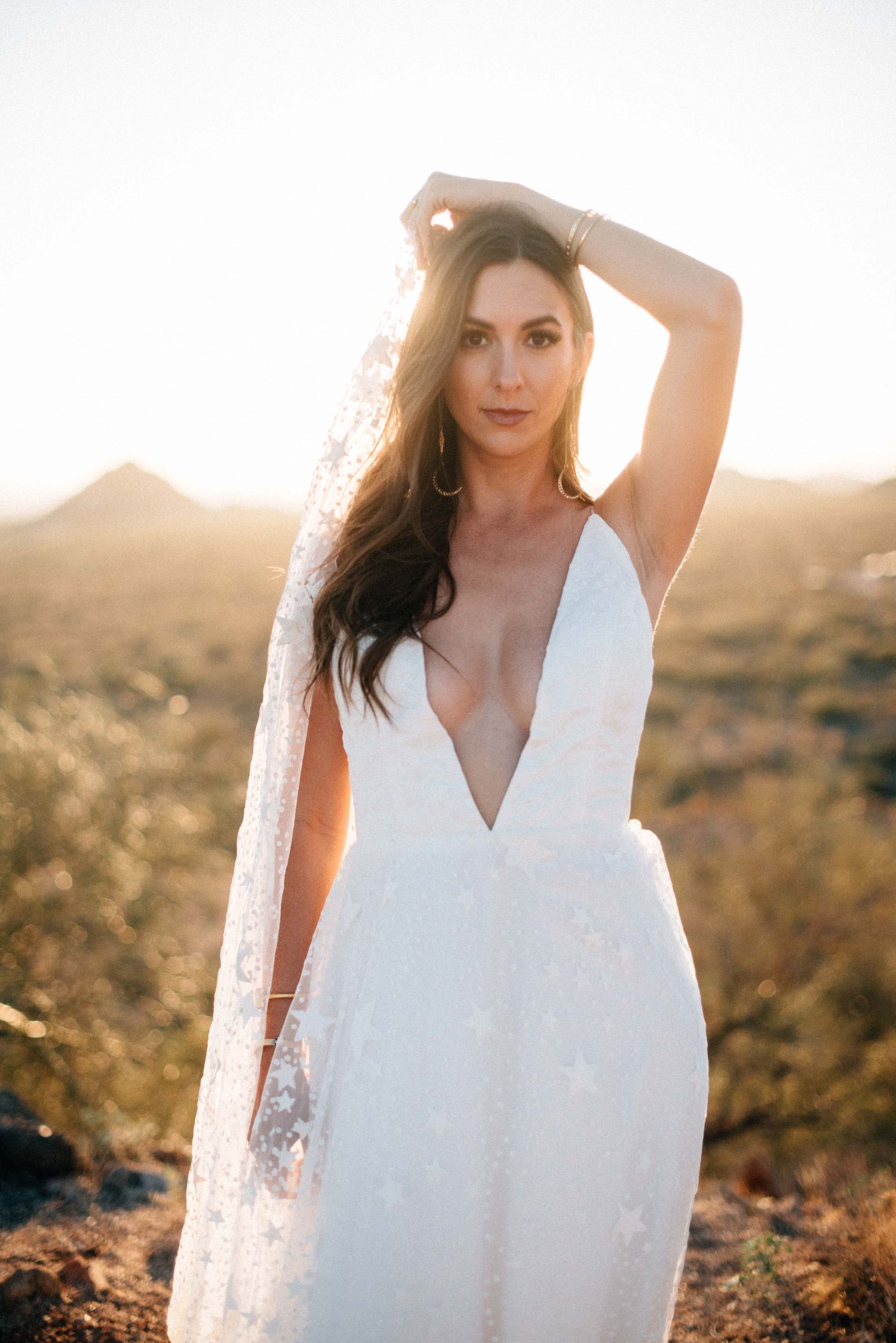 A woman in a white dress poses in golden sunlight during a sunset photoshoot in a natural outdoor setting.