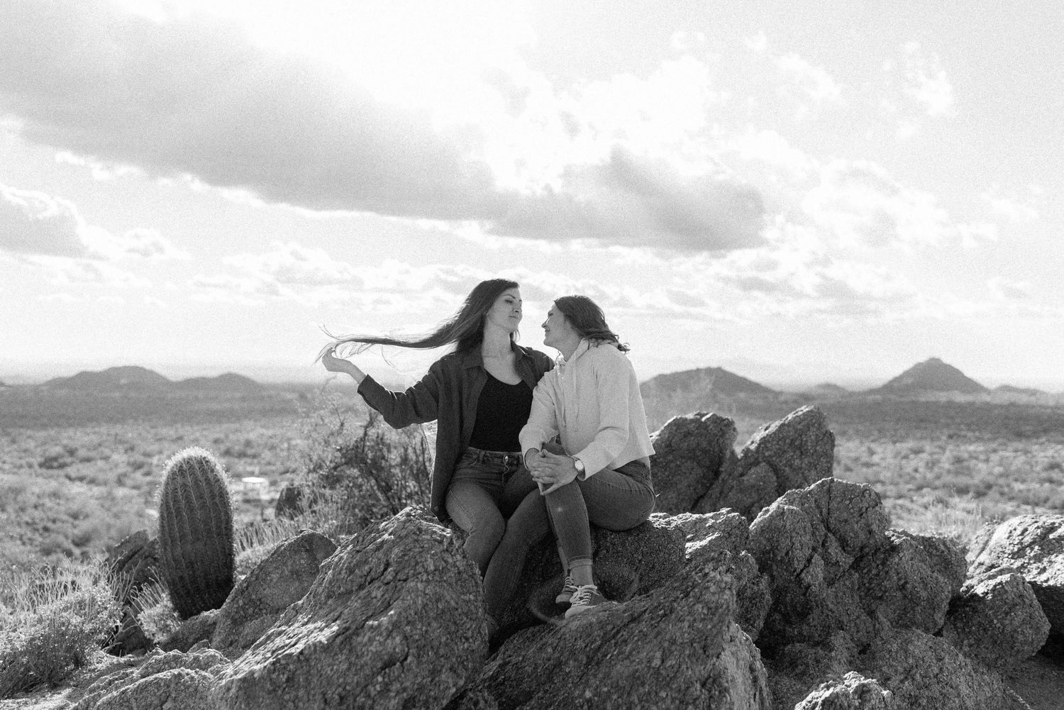 Black and white panoramic sequence shows a person climbing rocky mountain terrain against a cloudy sky.