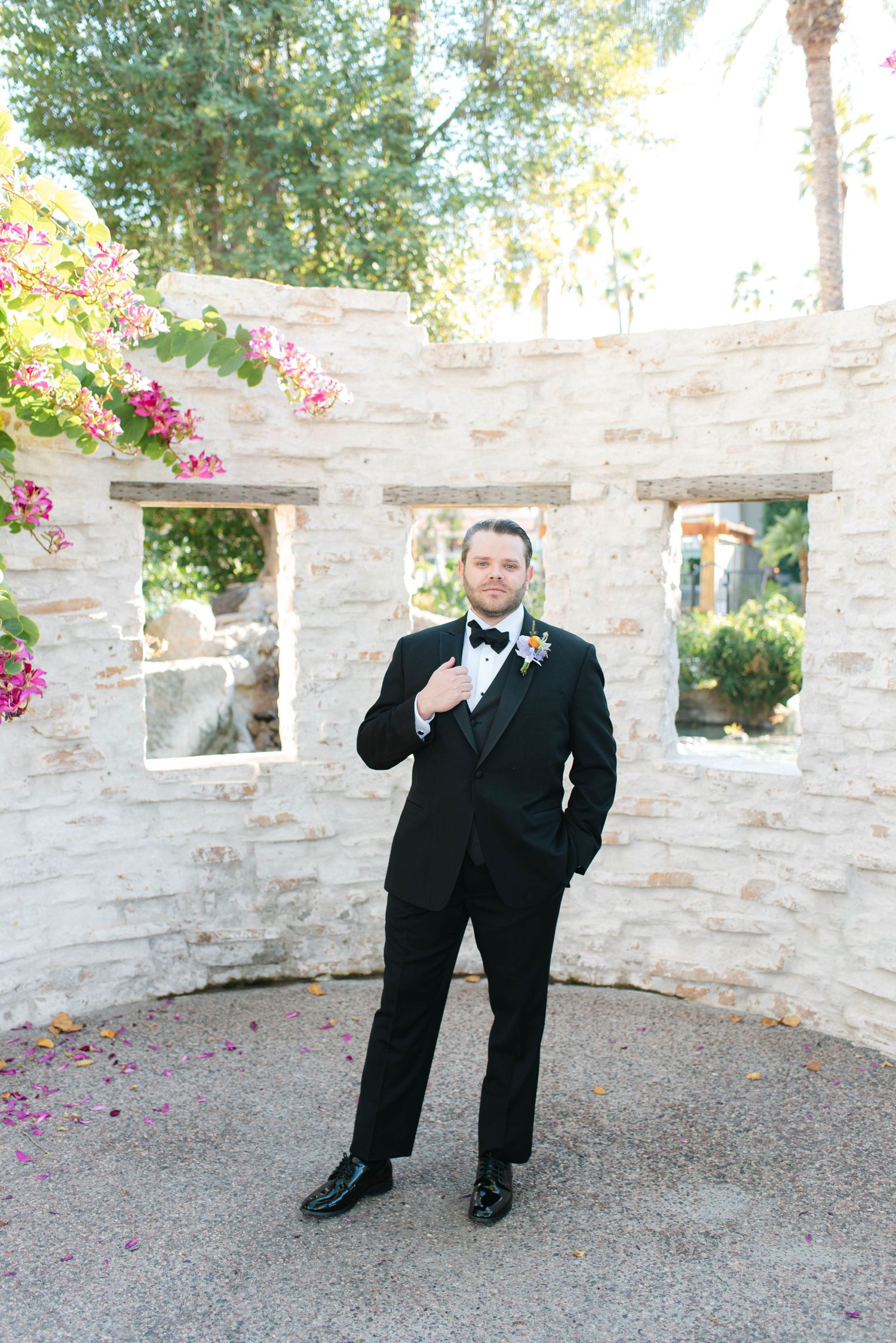 Four sequential photos show someone in a black tuxedo posing playfully against a stone wall with pink flowers.