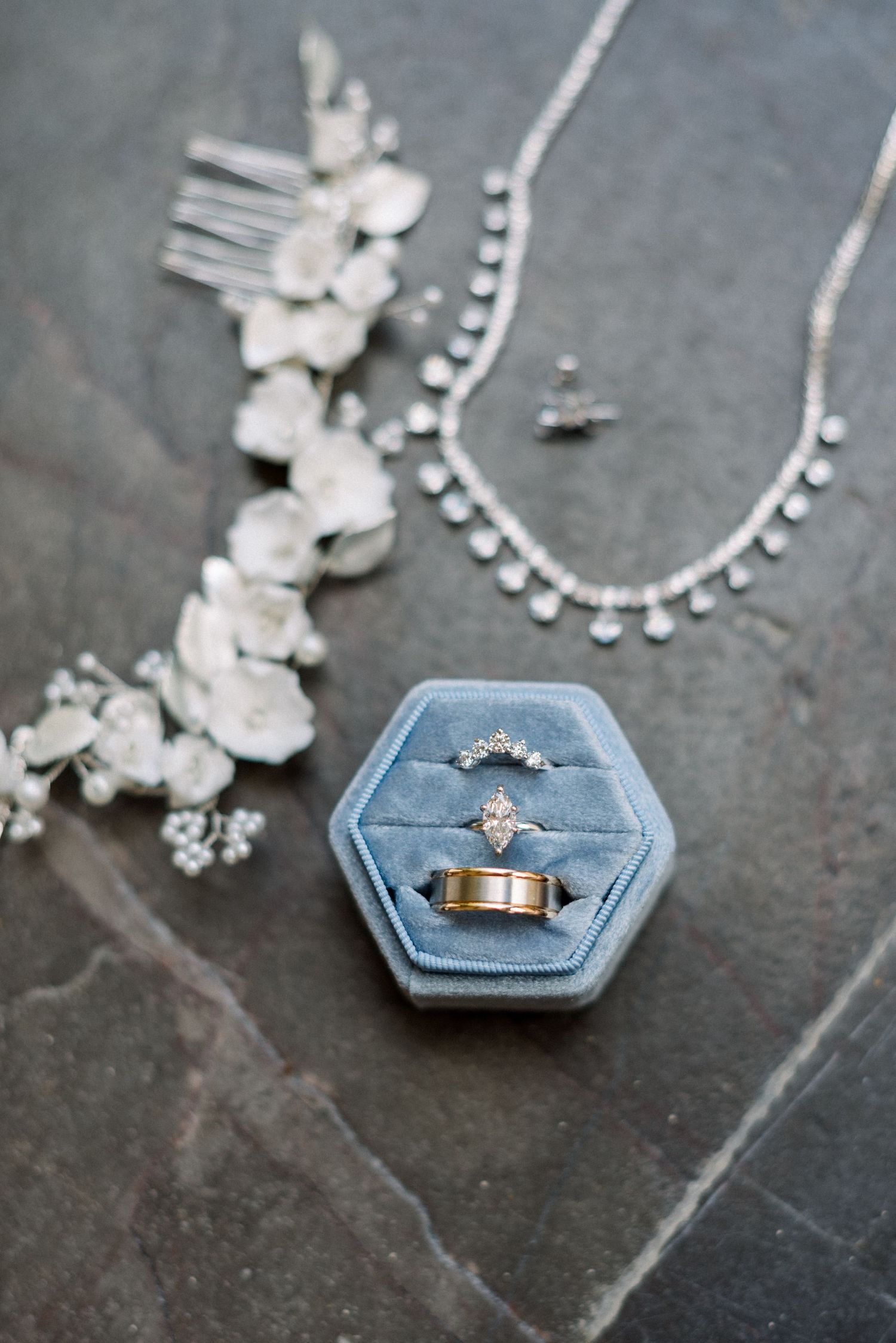 Wedding rings displayed in a blue hexagonal ring box with bridal accessories on dark surface.