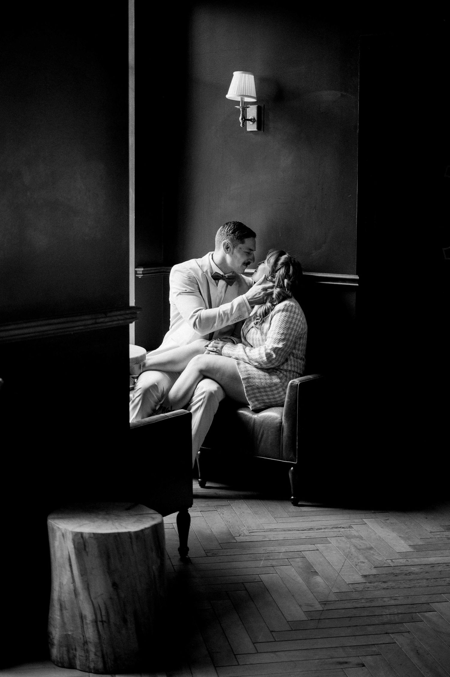 Dramatic black and white portrait of couple sharing intimate moment in dimly lit room.