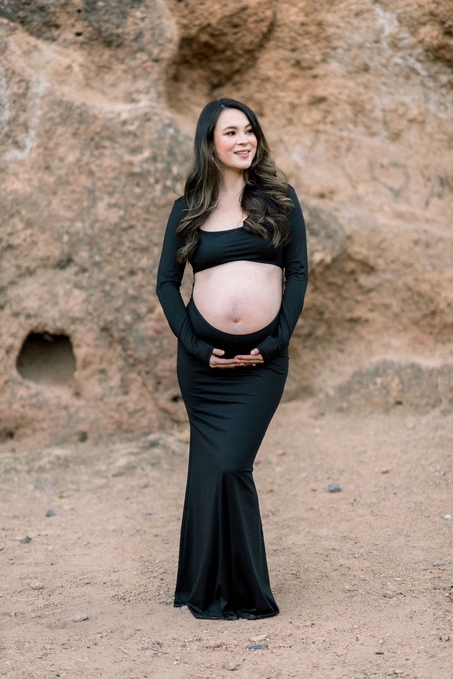 Maternity portrait in black two-piece dress against desert canyon wall.
