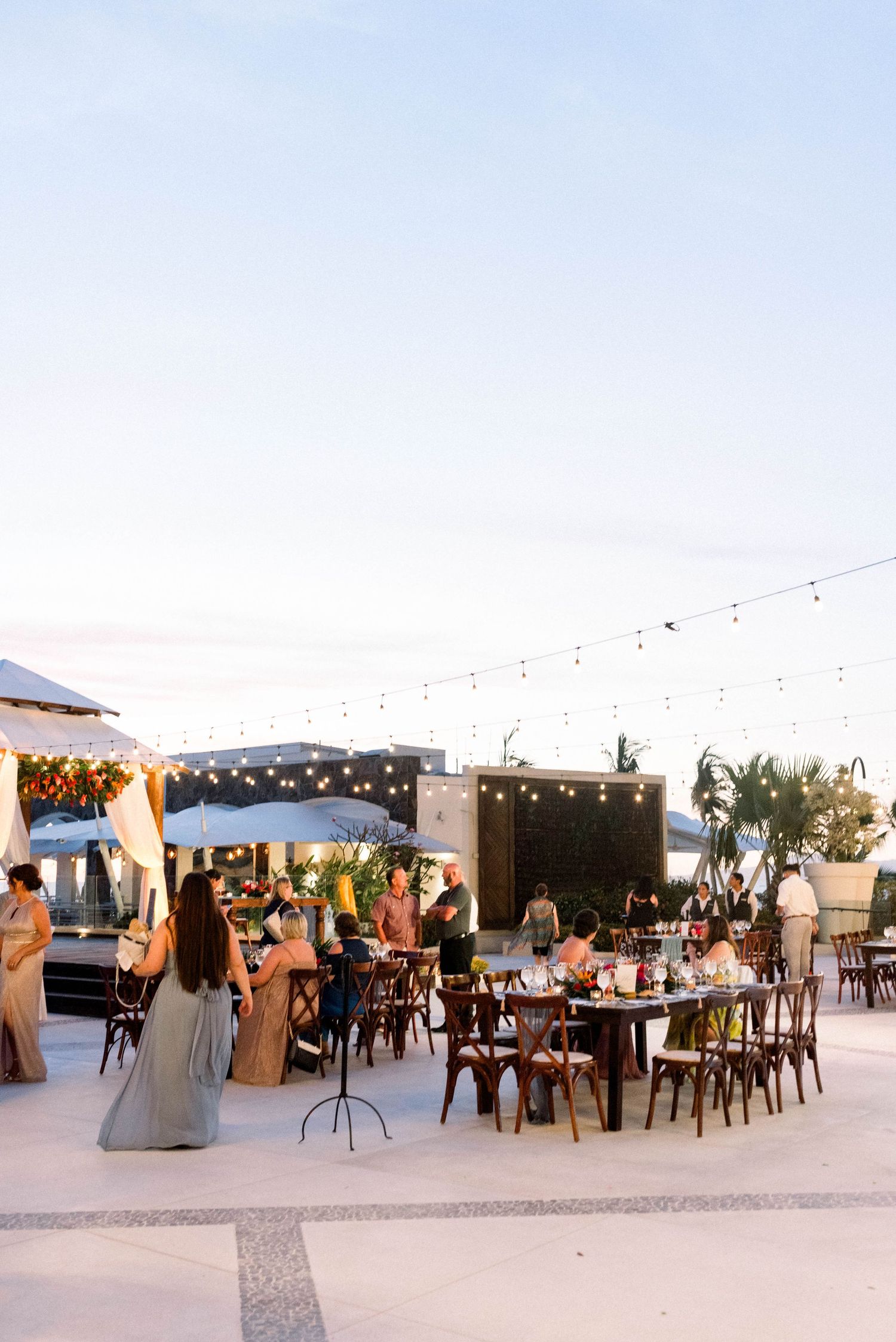 Outdoor evening reception venue with string lights and wooden chairs under twilight sky.