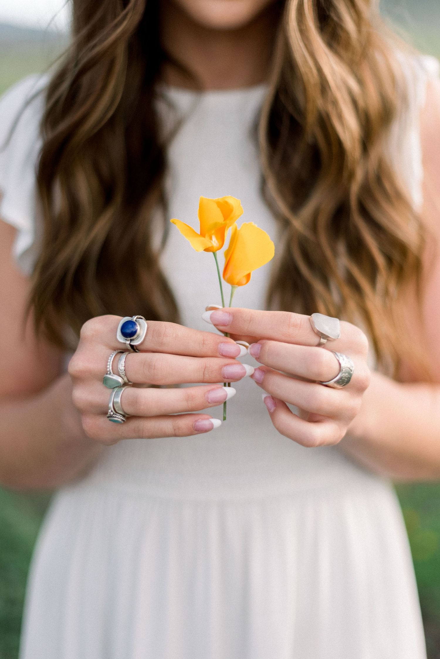 Hands holding yellow wildflowers show multiple rings against white dress.