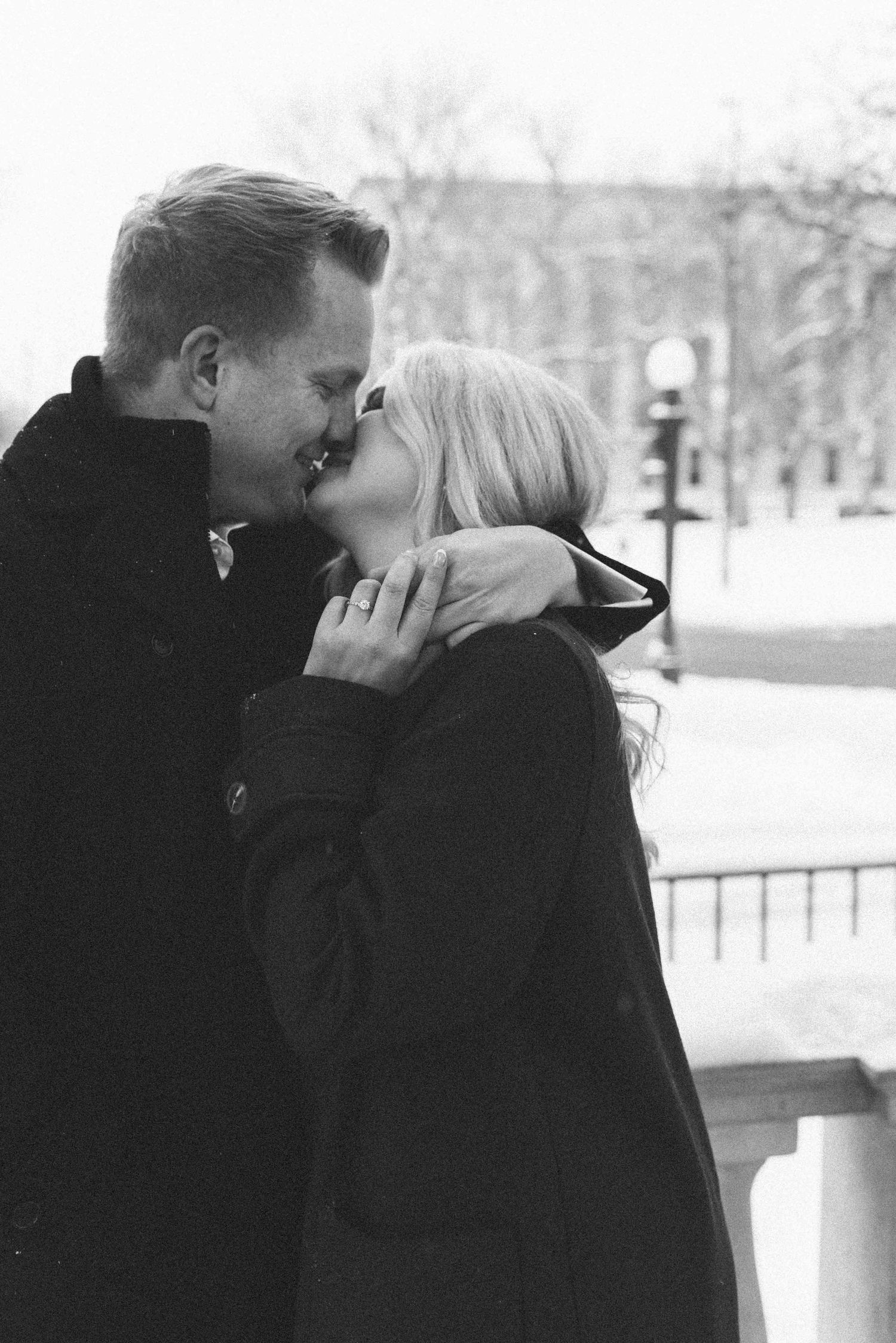 A close-up black and white photo of a couple sharing a romantic winter kiss.