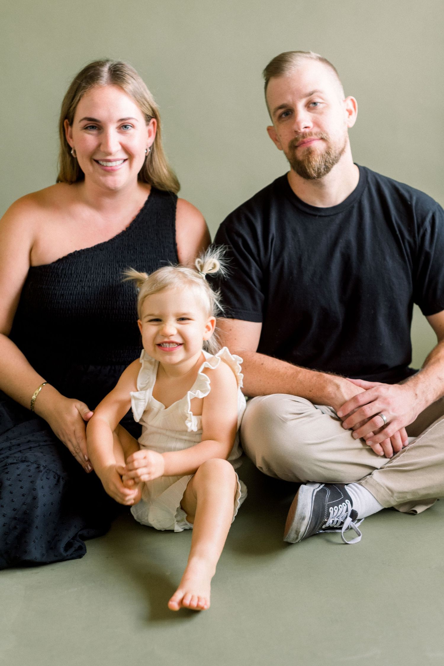 Happy family of three posing together during a studio photo session against a neutral wall.