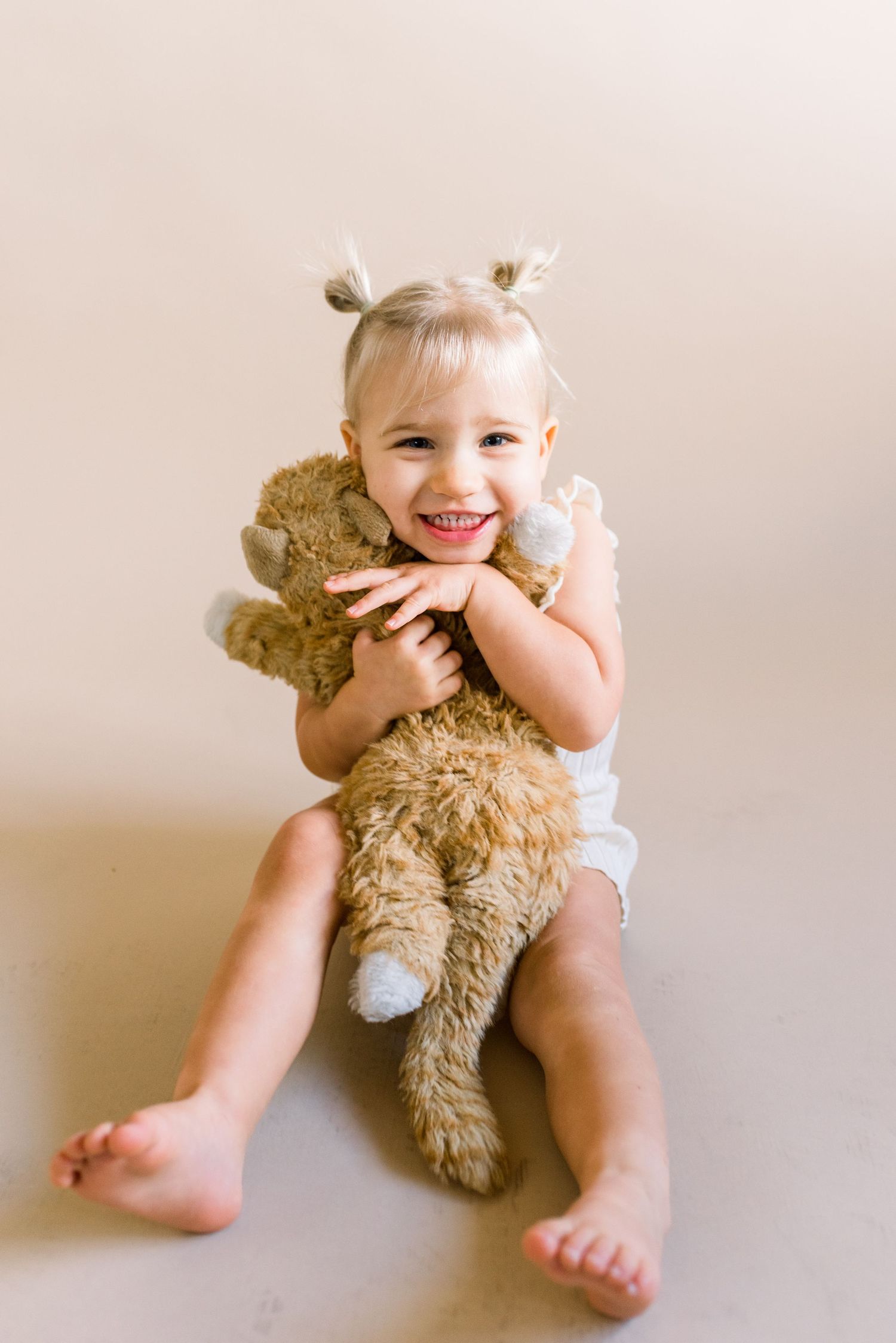 A playful youngster hugging a large teddy bear while sitting on floor.