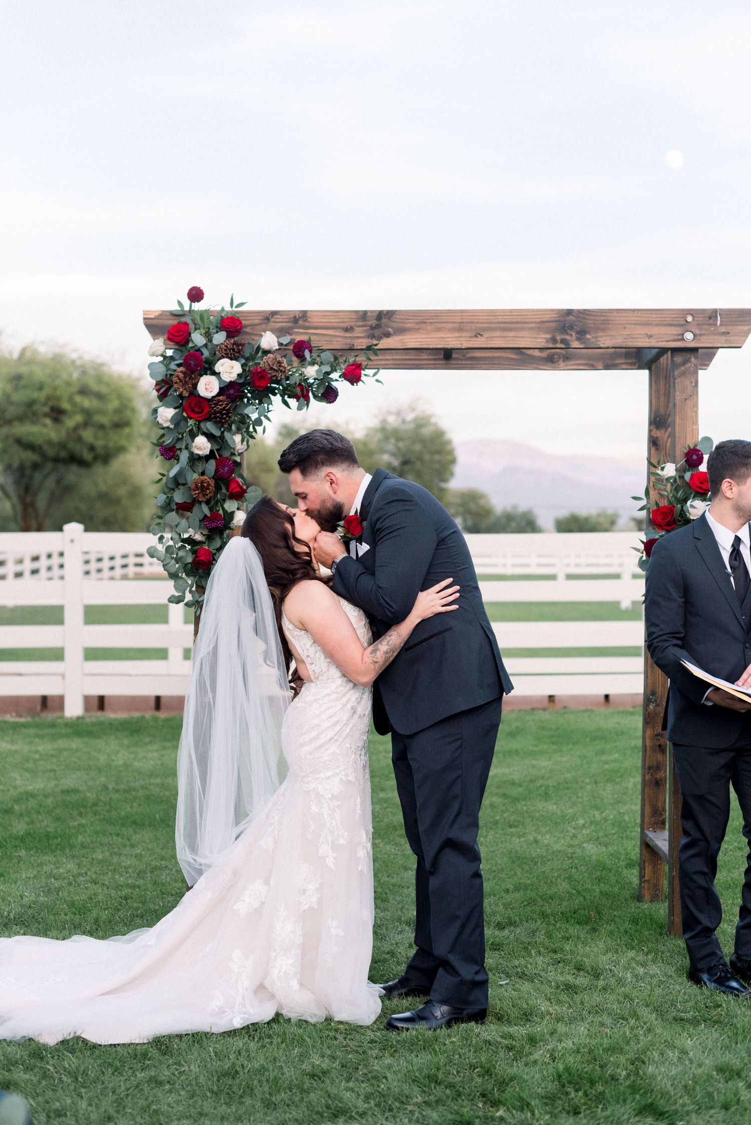 A romantic first kiss moment under a rustic wooden arch decorated with red roses.