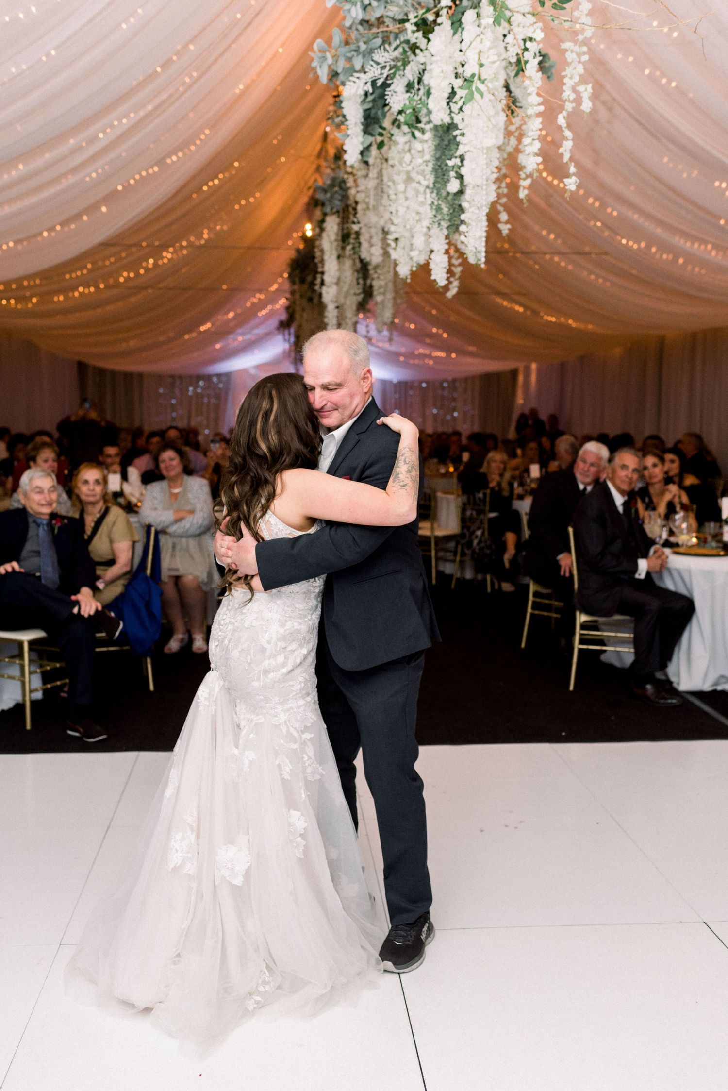 Couple sharing an intimate first dance at wedding reception under white draped ceiling with floral decor.