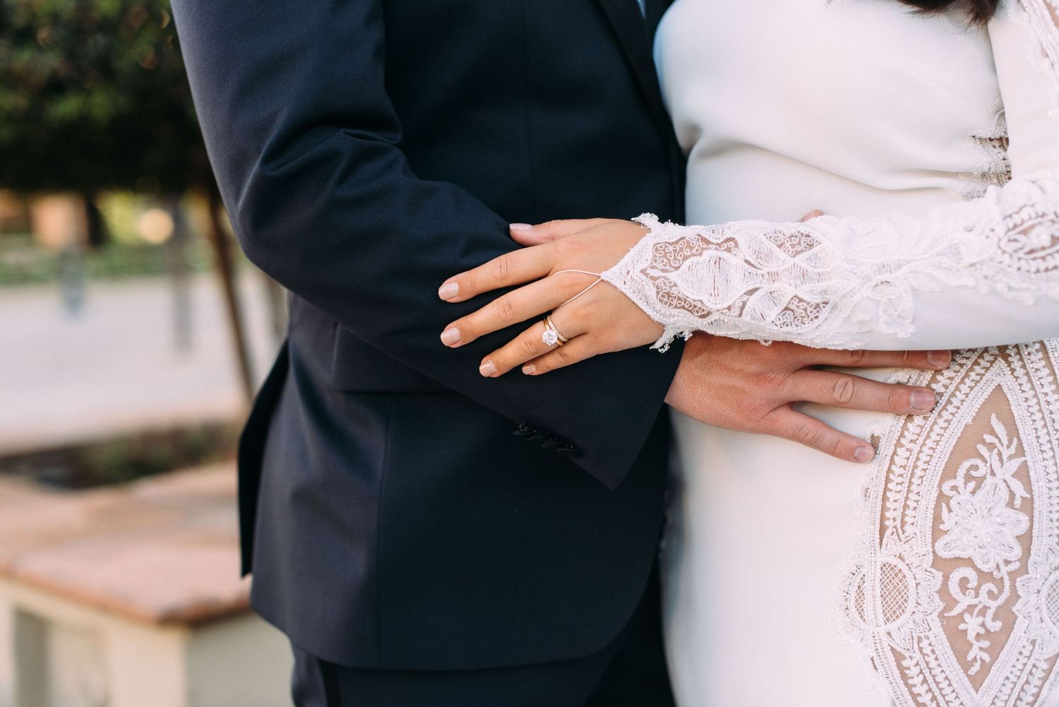 Close-up of couple's hands showing wedding rings and lace dress details.