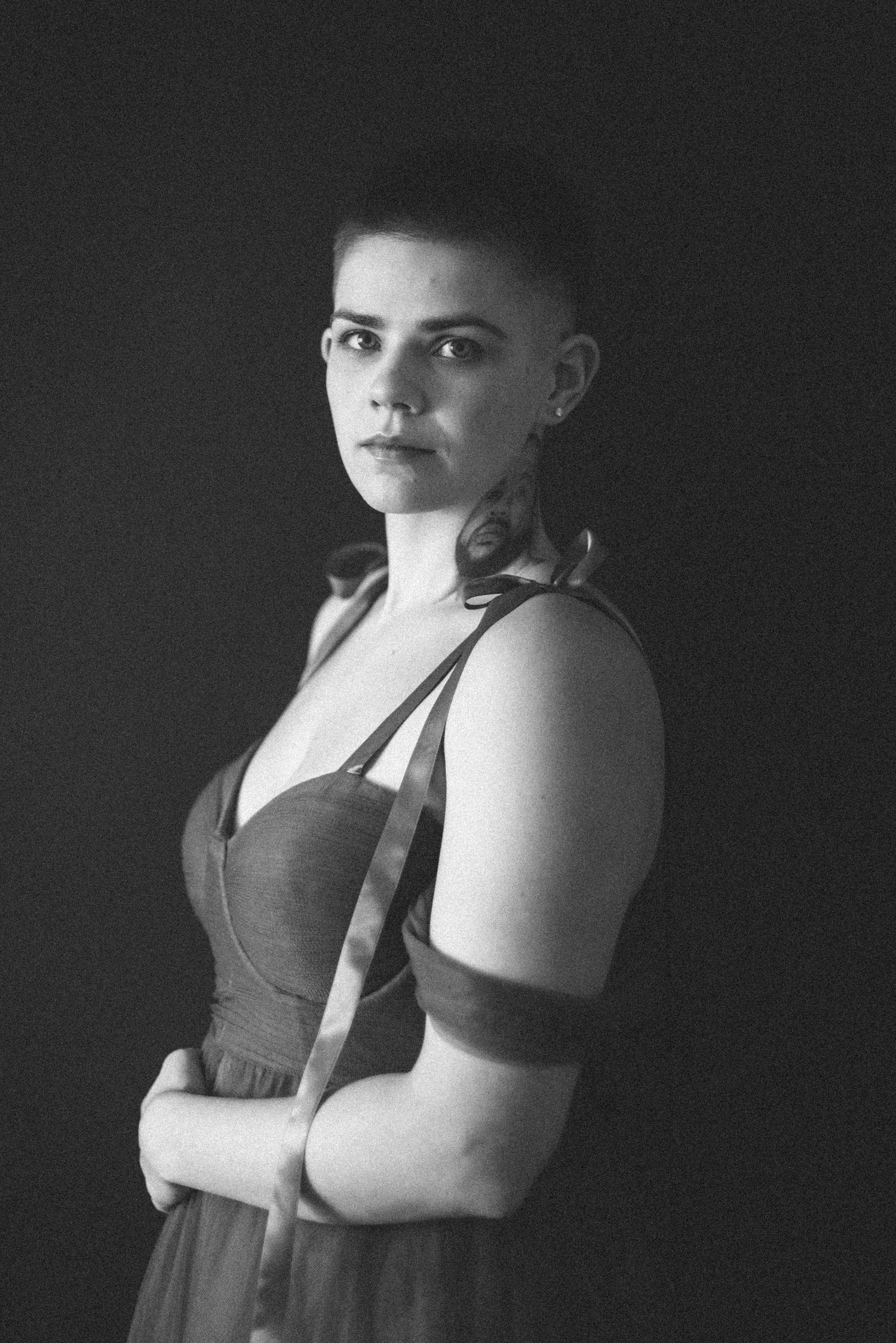 Black and white portrait of a person wearing a sleeveless brown dress against a dark background.