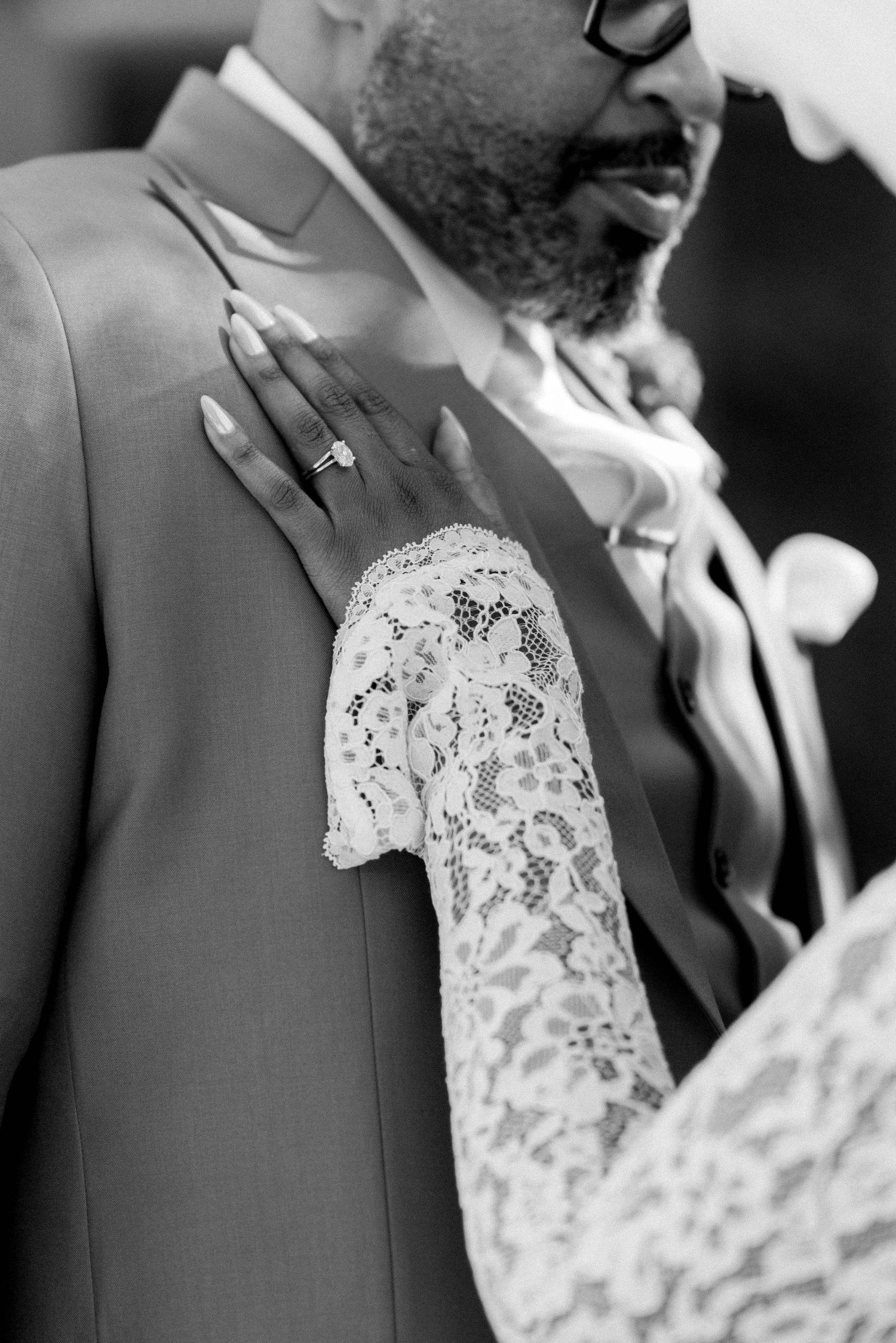 Black and white wedding photo showing a tender moment with lace dress detail and engagement ring.