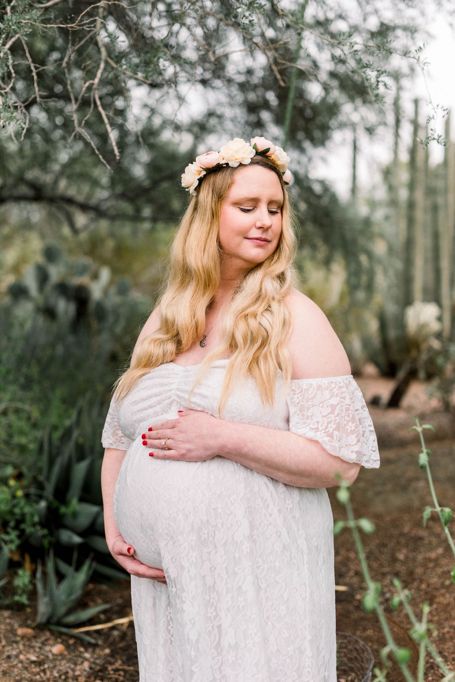 Serene maternity portrait with white off-shoulder dress in a desert botanical setting.