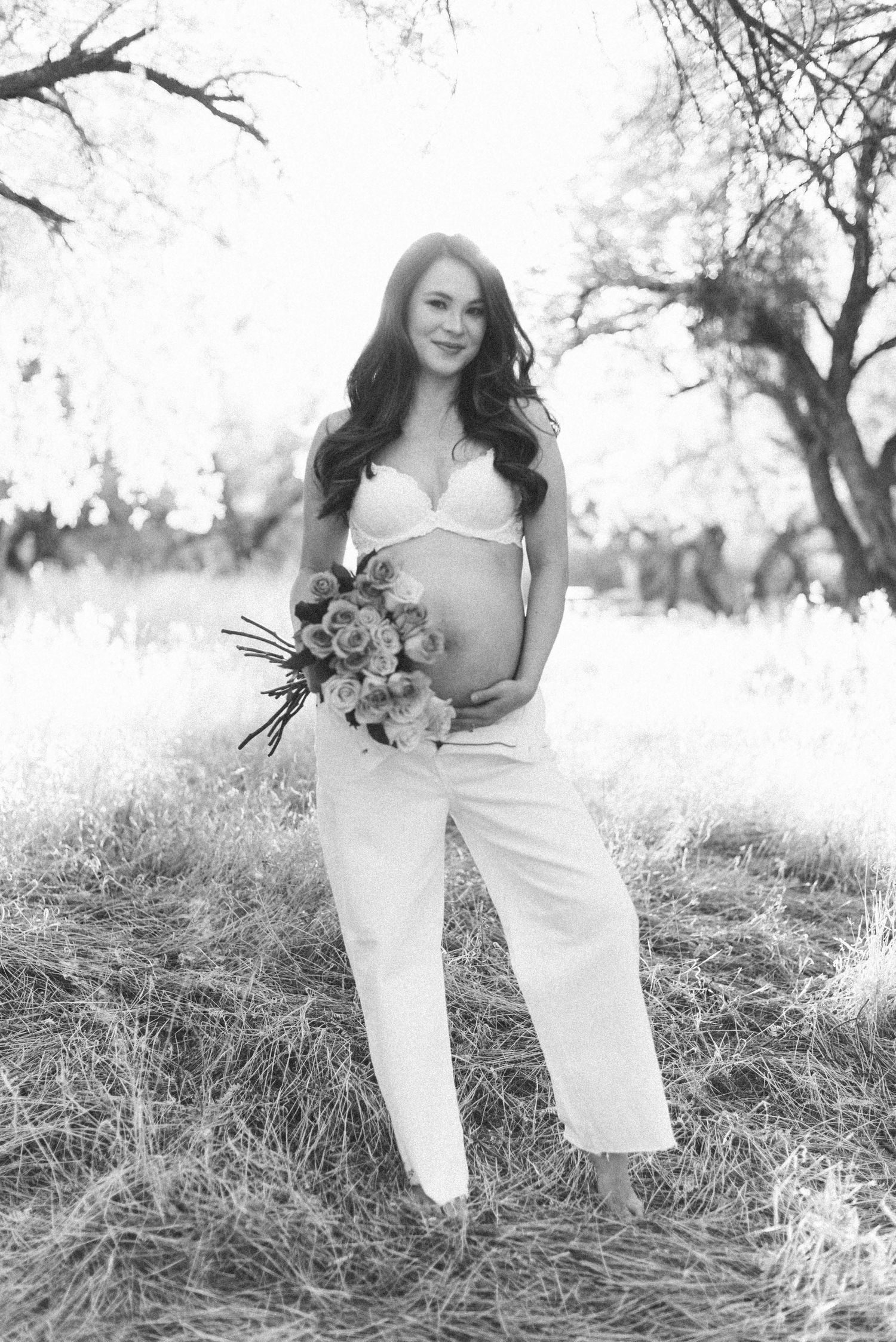 Maternity photoshoot in dreamy black and white with roses in a sunlit field.