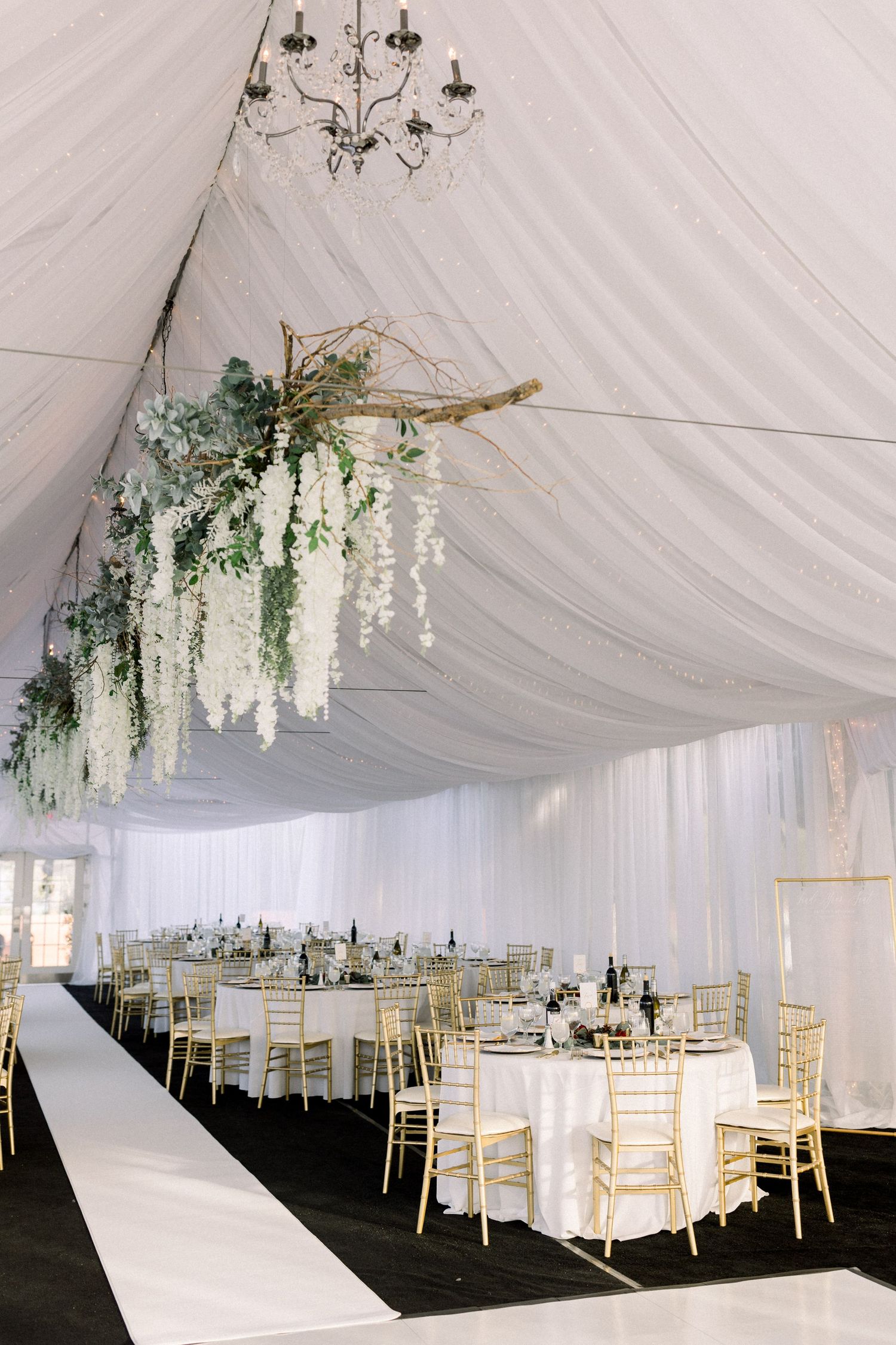 White reception tent with hanging floral arrangements and gold chiavari chairs.