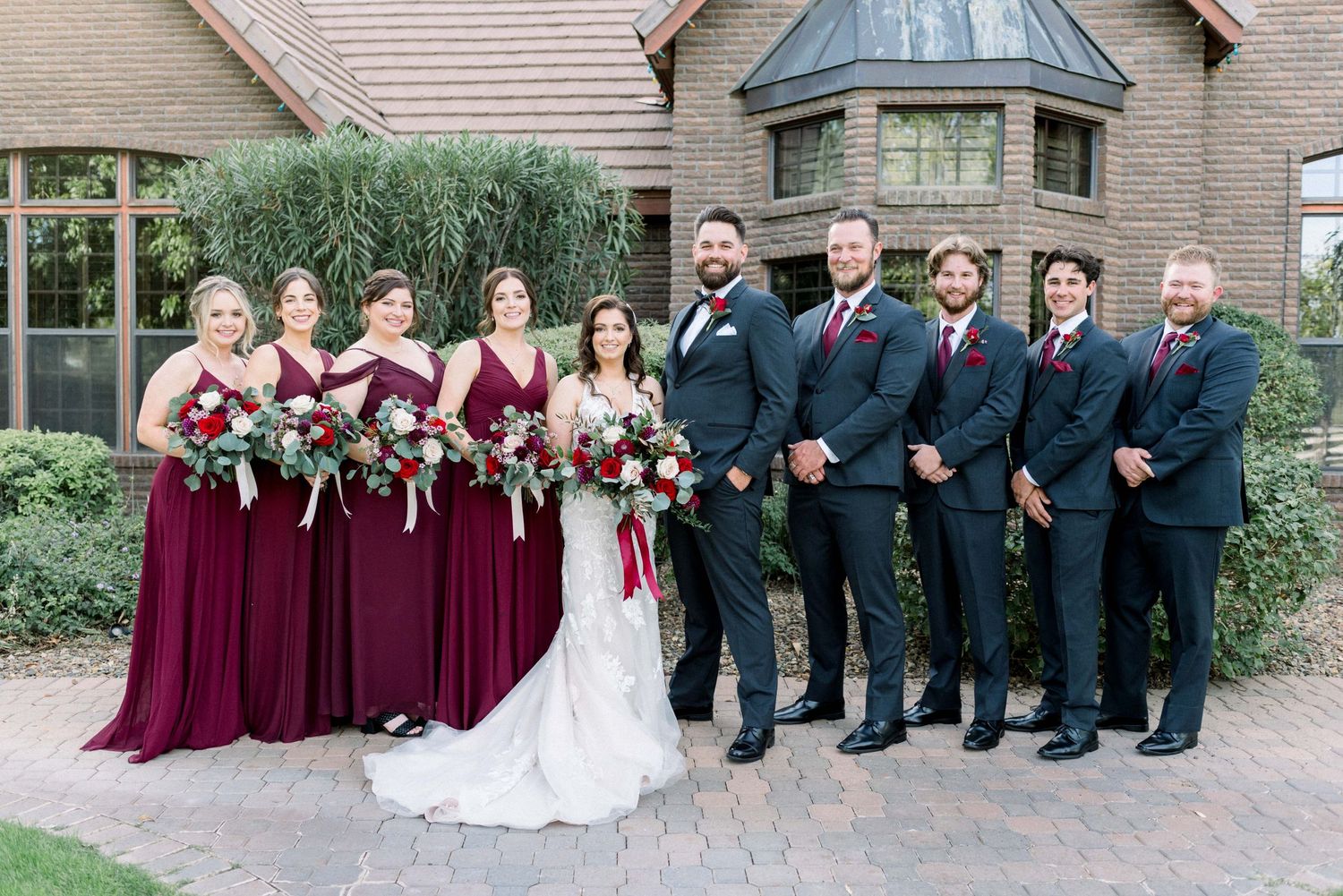 Wedding party in burgundy dresses and navy suits pose together outside a brick venue.