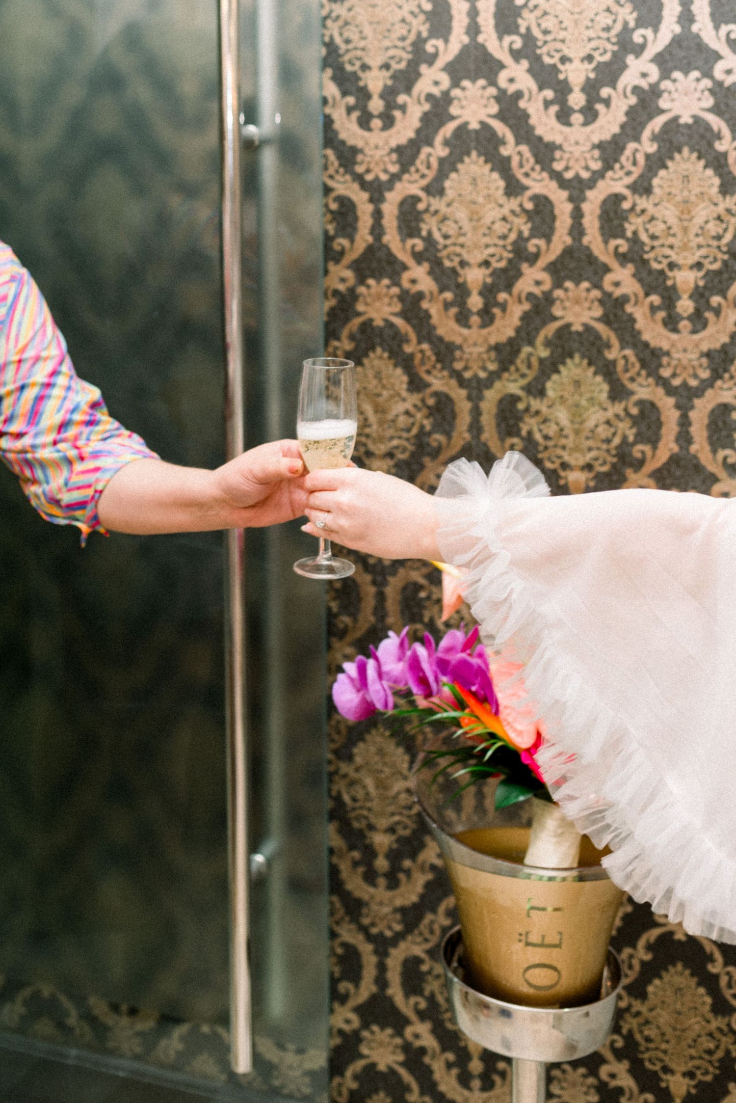 Champagne toast with floral arrangements against damask wallpaper at a wedding event.