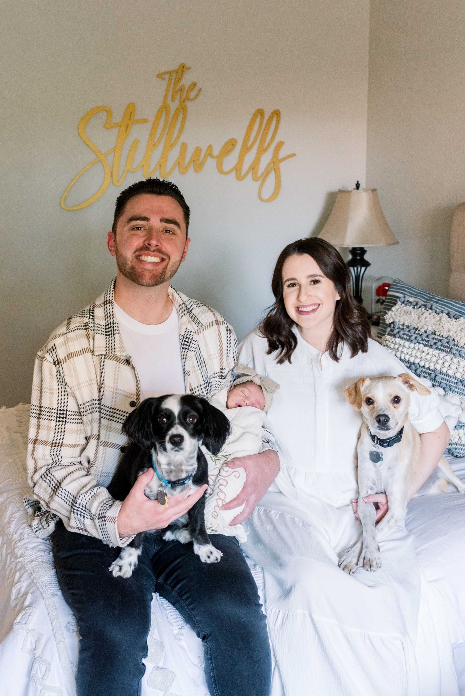 Family portrait with newborn baby and two dogs beneath gold 'The Stillwells' wall text.