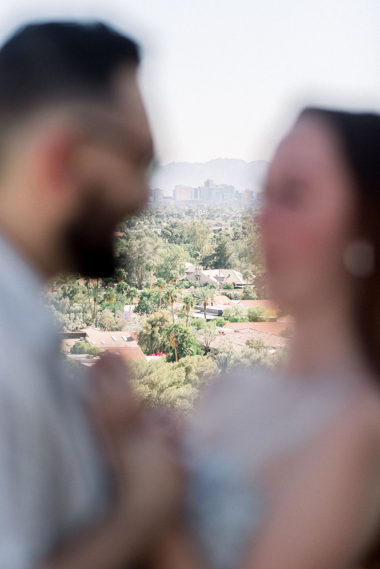 Blurred couple in foreground with cityscape and gardens visible in background through soft focus.