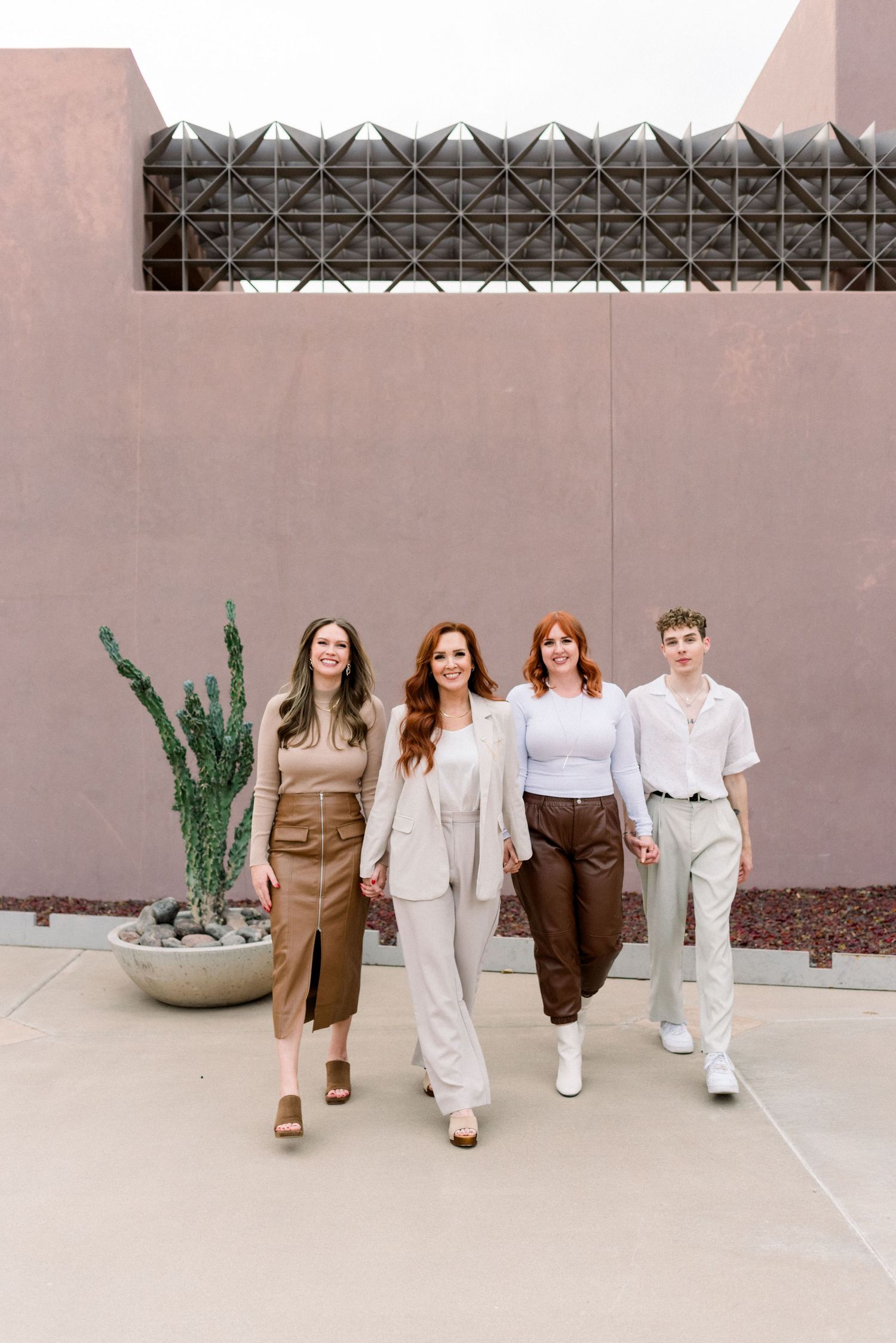 A group of people walking in a line wearing coordinated brown and white outfits against a pink wall.