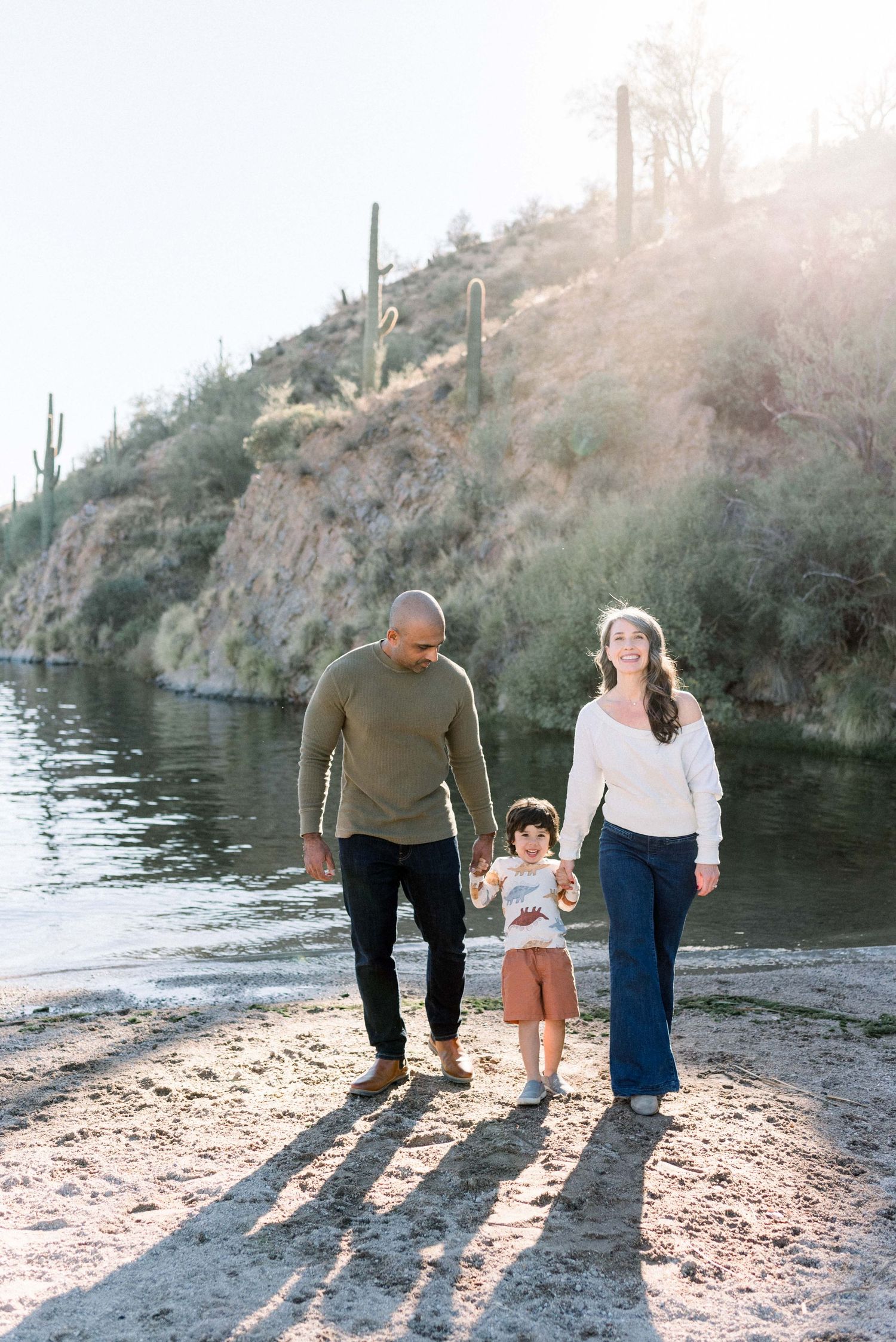 Family walking together along desert lake shore at sunset casting long shadows on sandy beach.