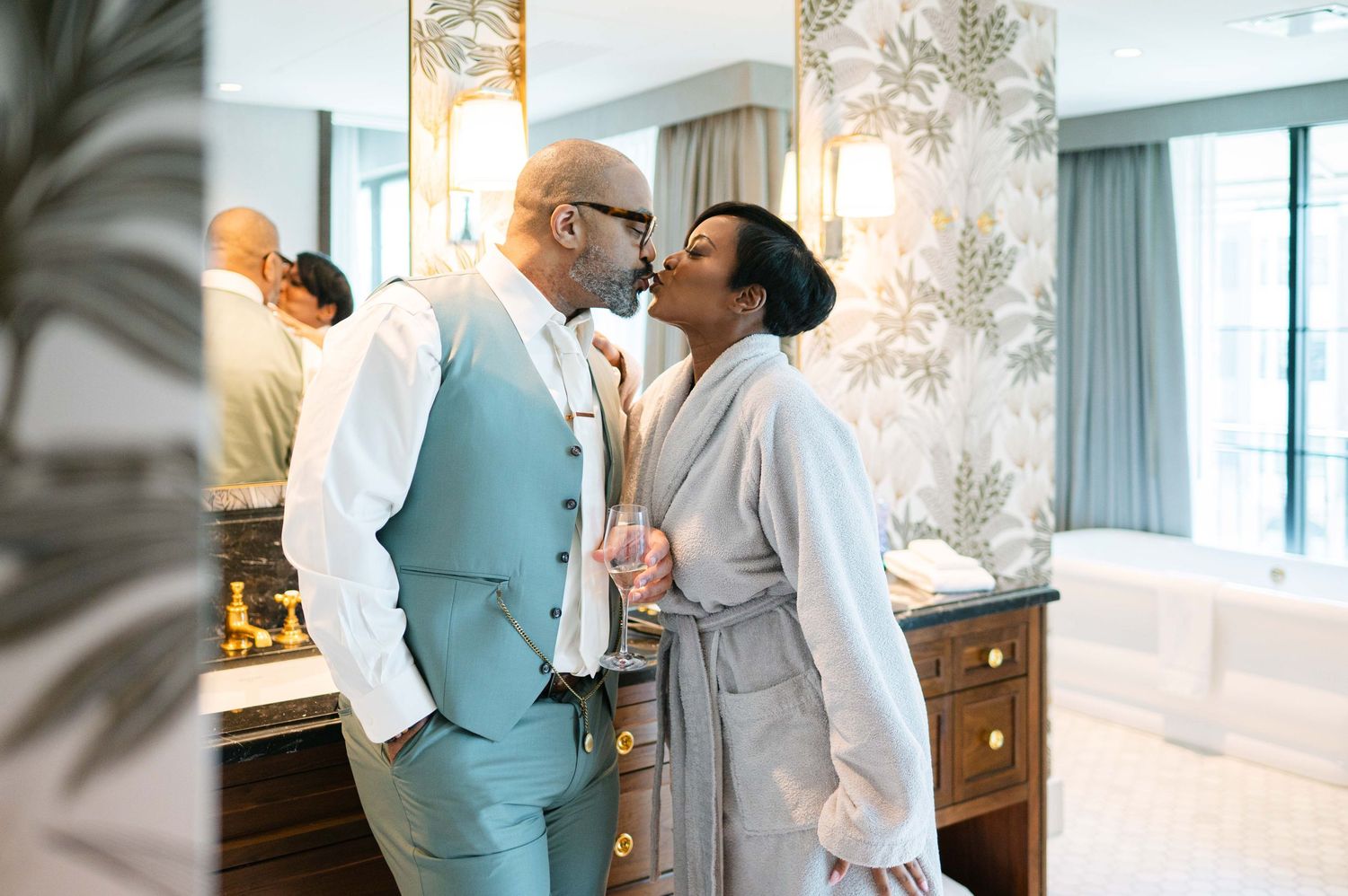 A couple shares an intimate moment in a bathroom, with one person wearing a light blue vest and white shirt.