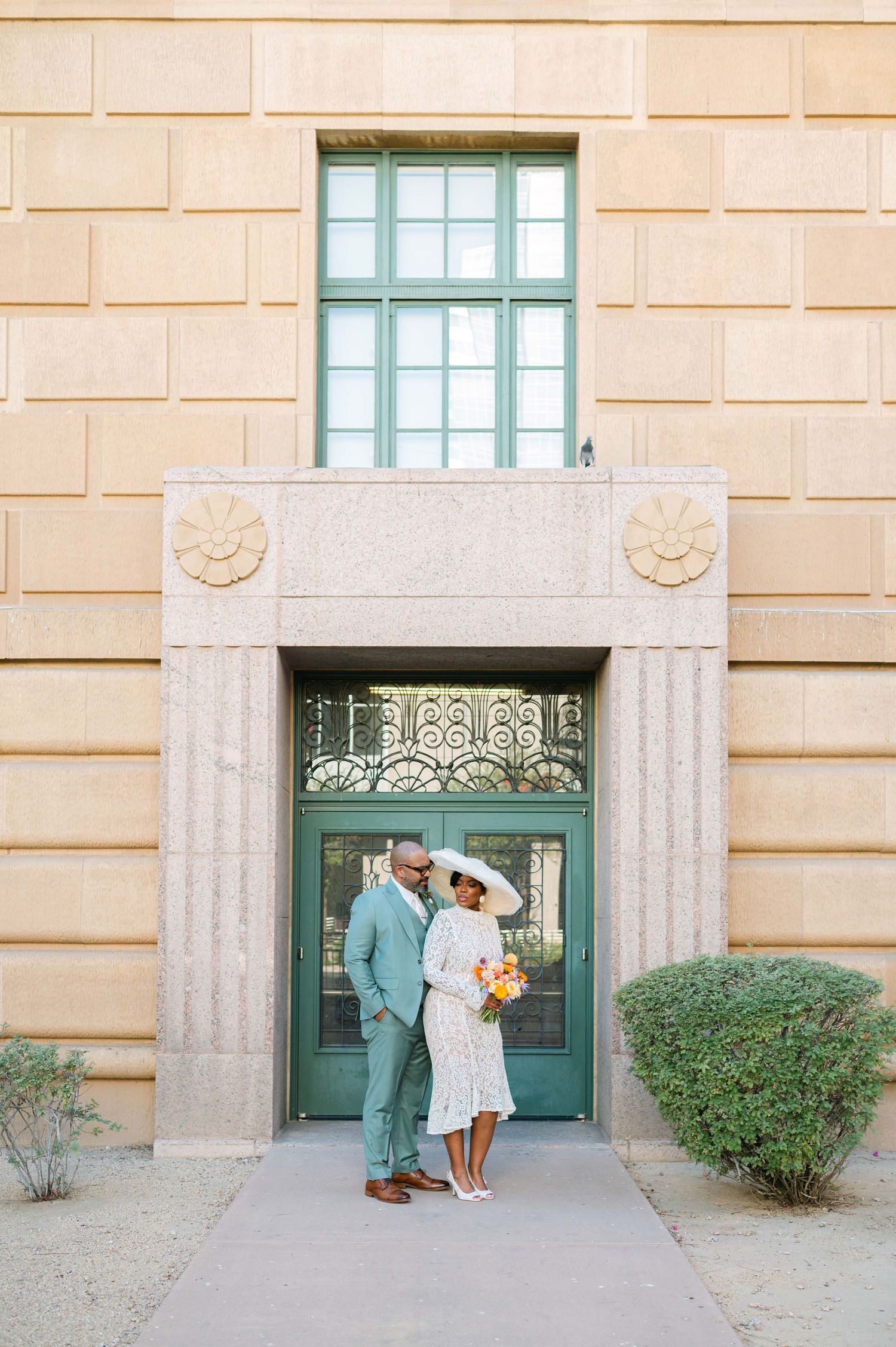 A couple poses under an ornate doorway entrance with green trim and decorative stonework details.