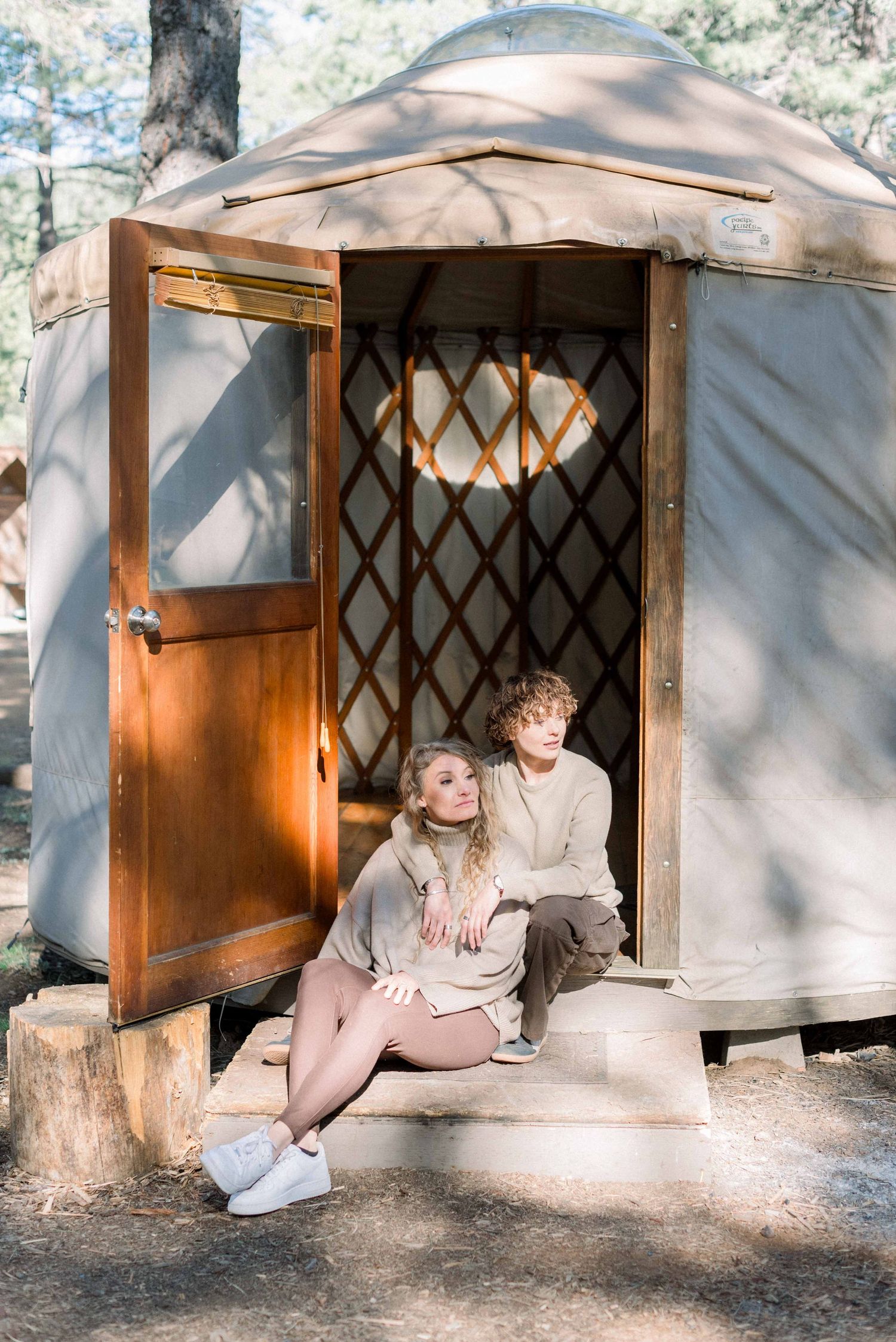Couple sitting in doorway of wooden yurt surrounded by forest.
