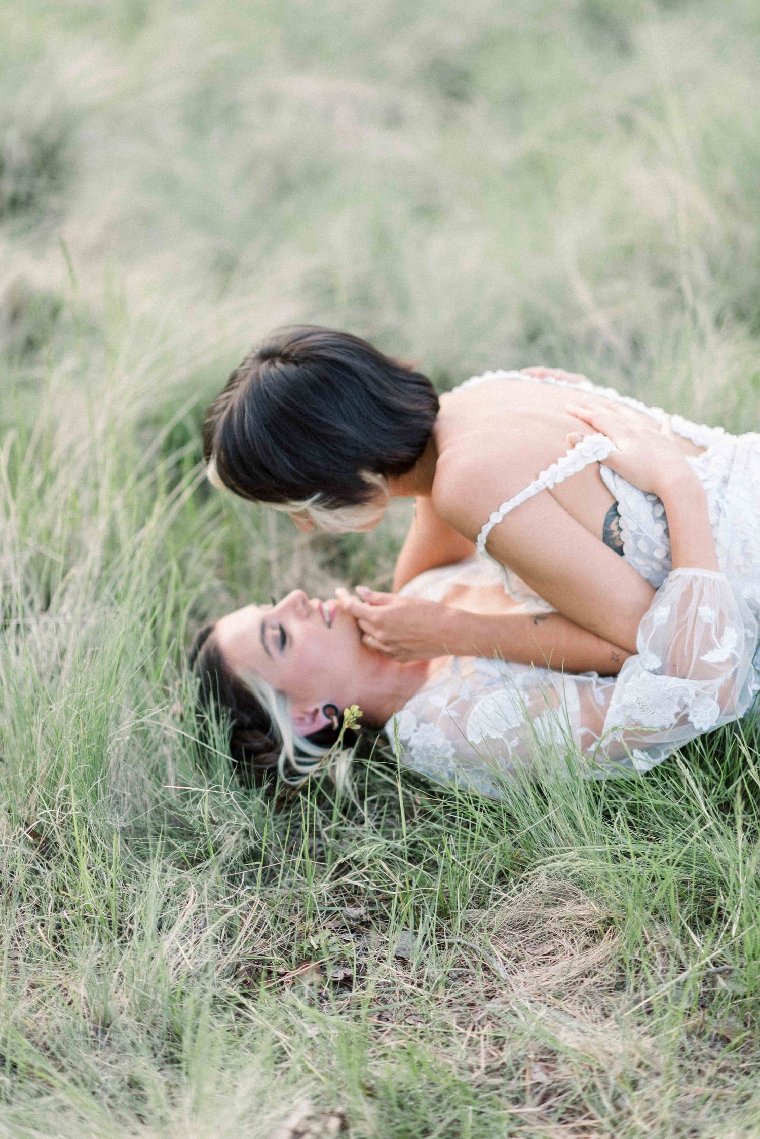 Joyful moment between couple in white dresses laying in tall grass.