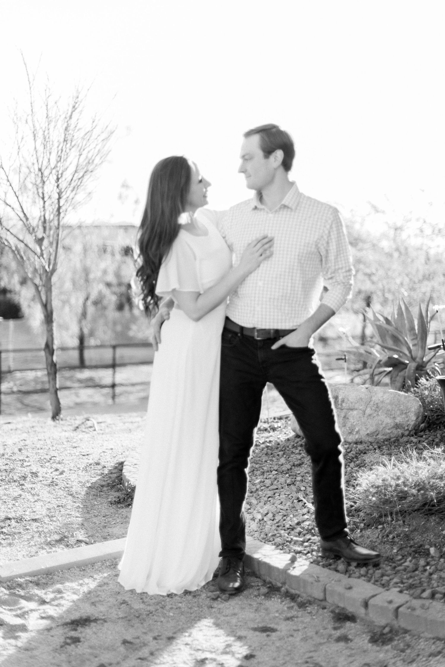 Black and white portrait of couple in elegant attire standing in garden setting.