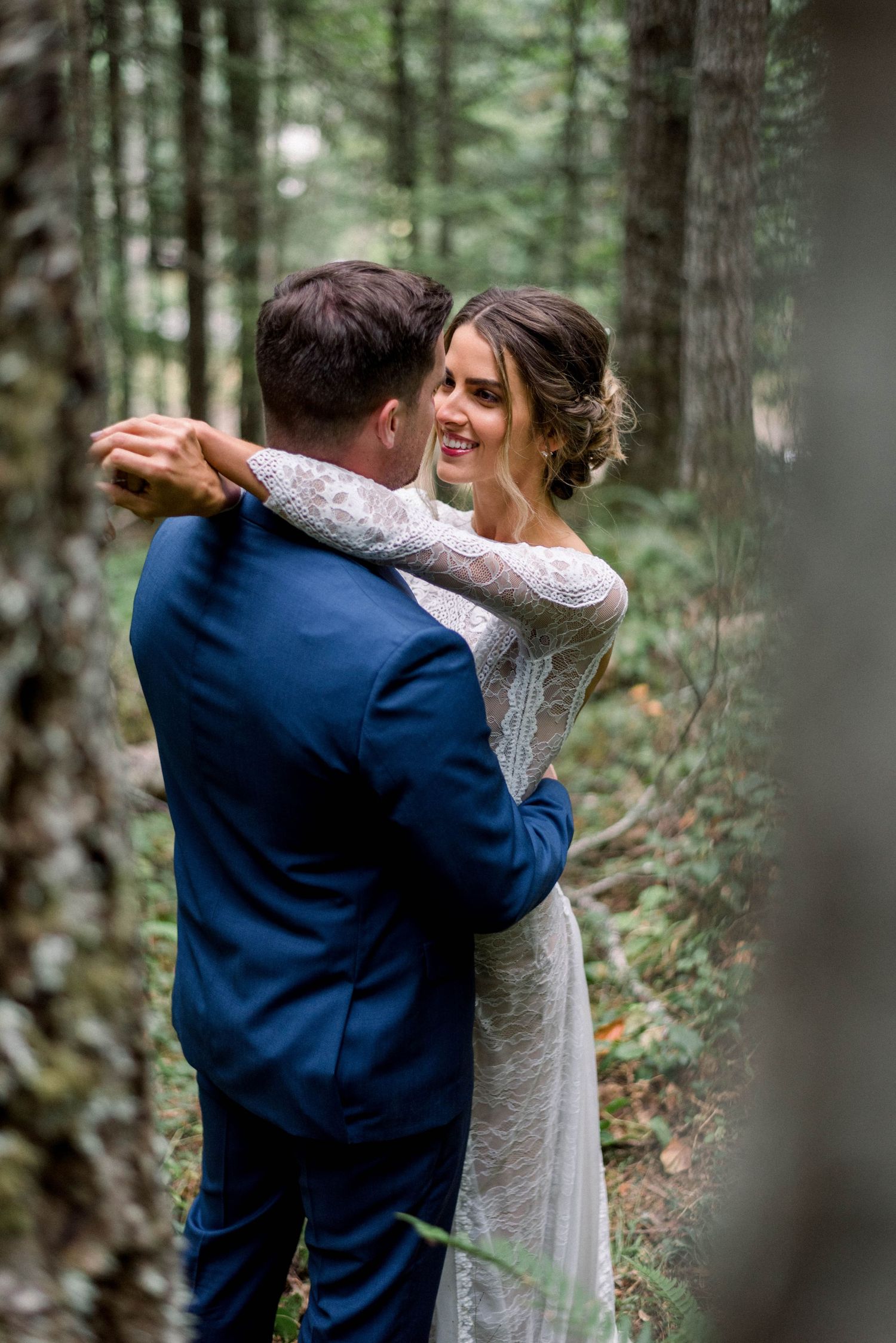 A couple share their first dance surrounded by tall trees in an outdoor forest setting.