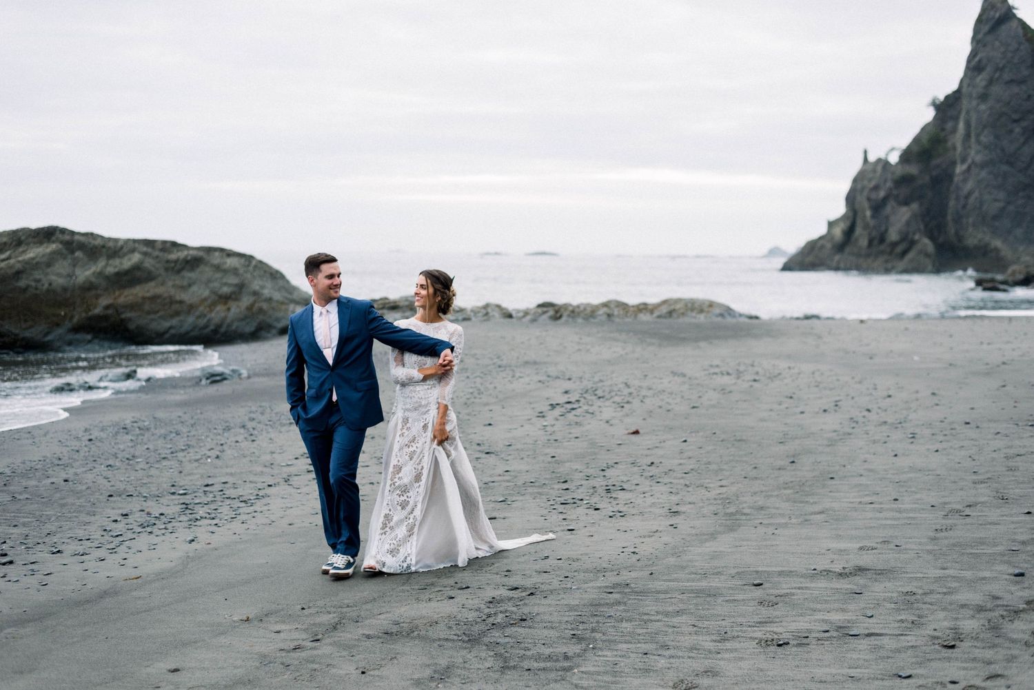A couple shares a dance on a dramatic coastal beach with rocky cliffs.