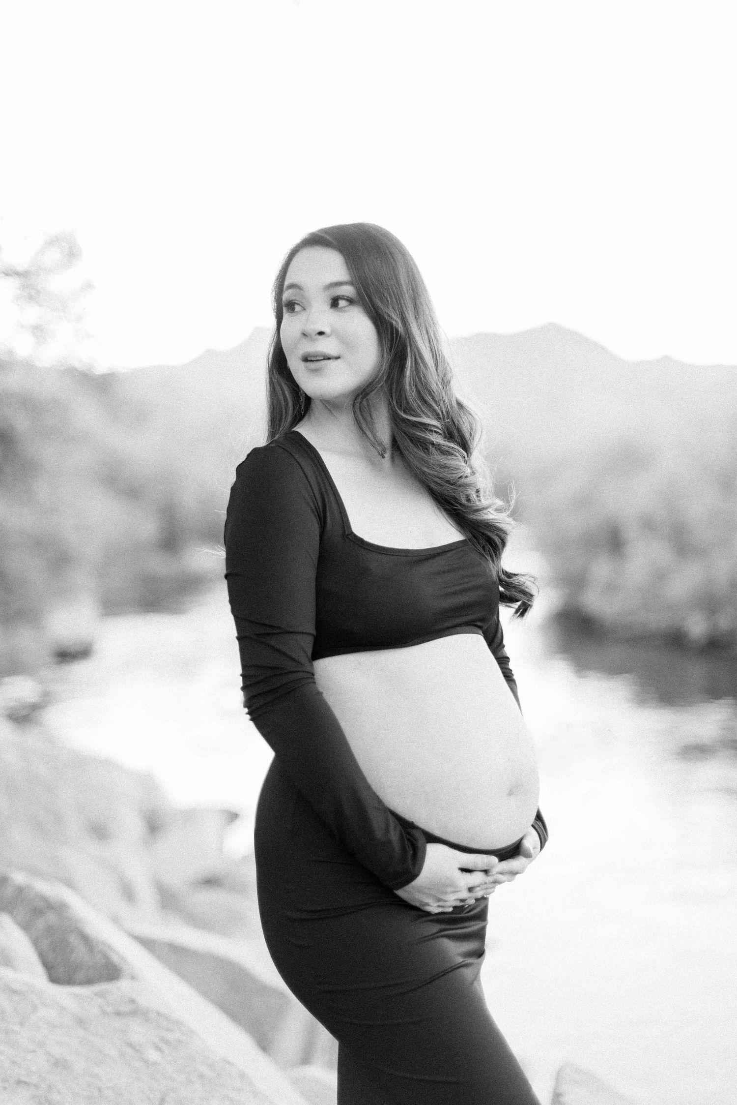 Black and white maternity portrait with mountain landscape backdrop.