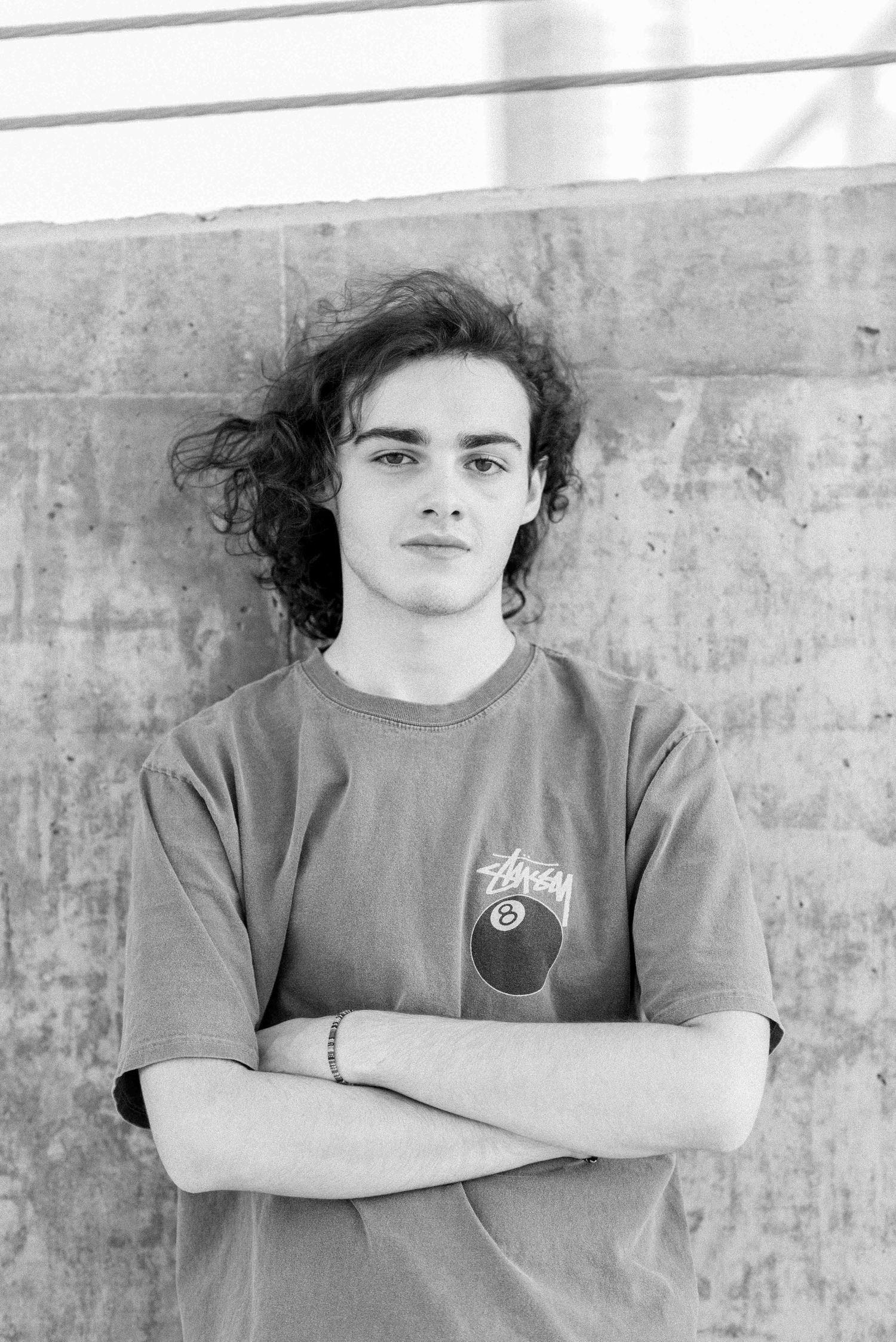 Black and white portrait of person in Stussy t-shirt against concrete wall.