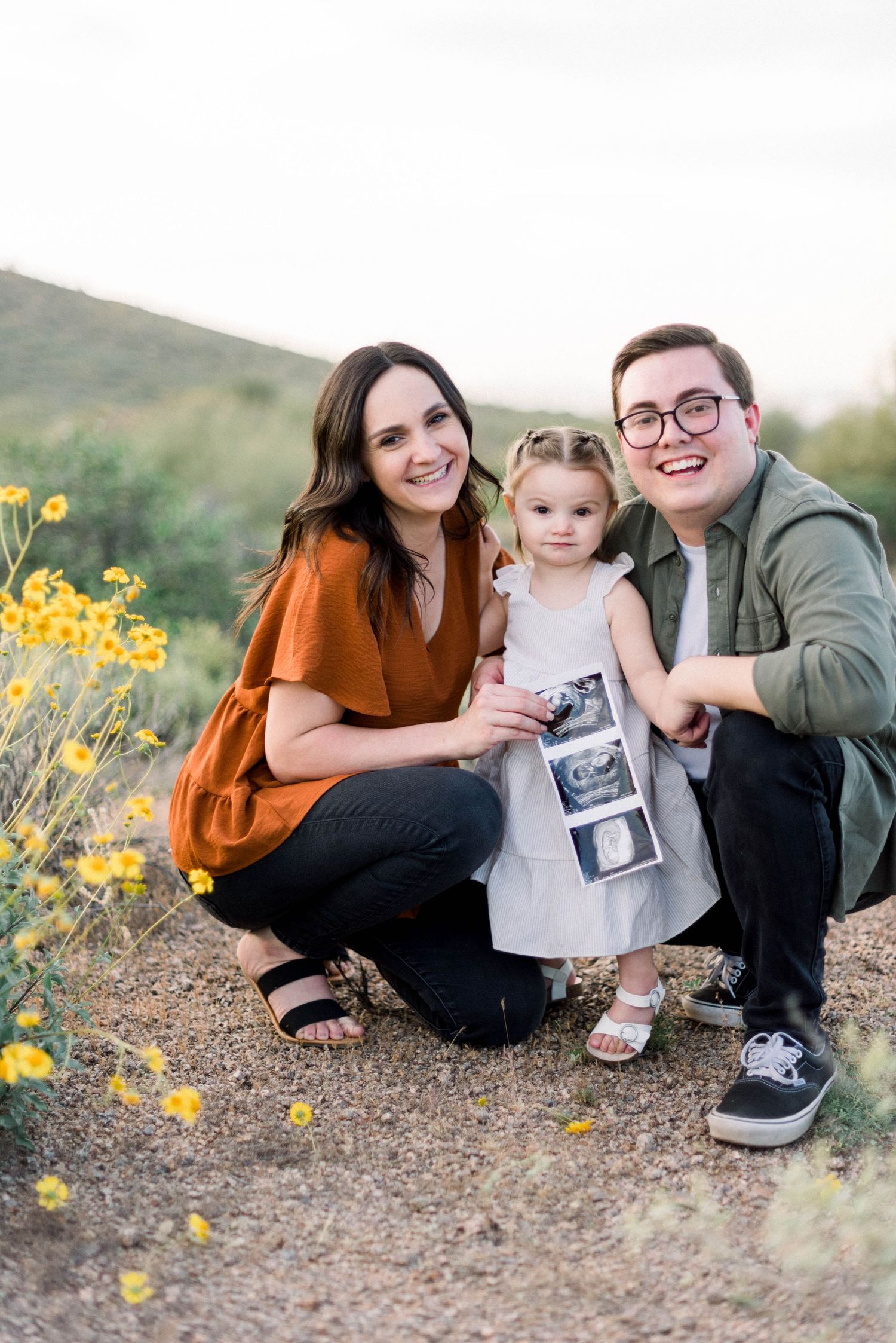 Family pregnancy announcement photo with ultrasound images in desert setting.