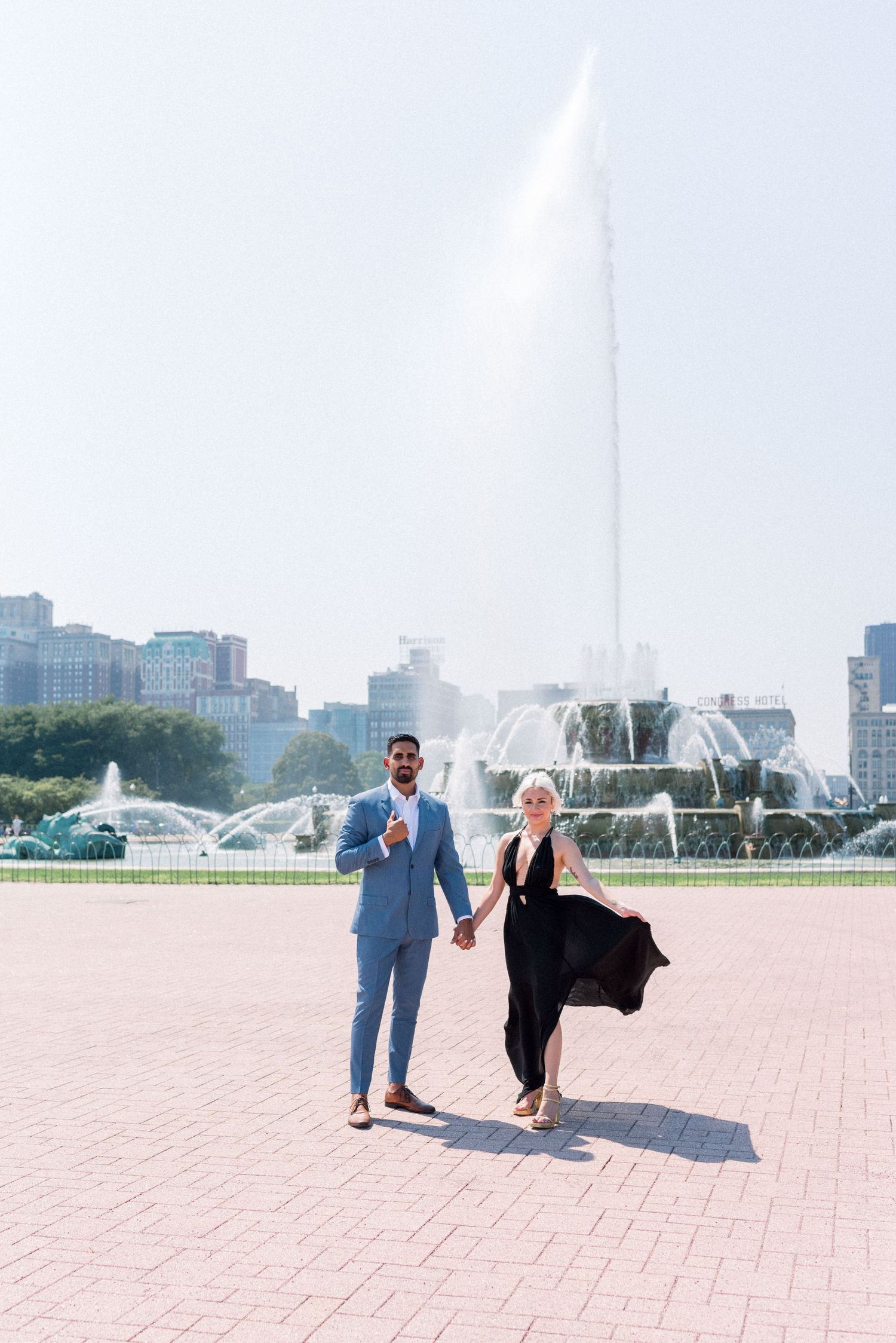 Couple walking hand in hand near iconic Chicago fountain with skyline in background.