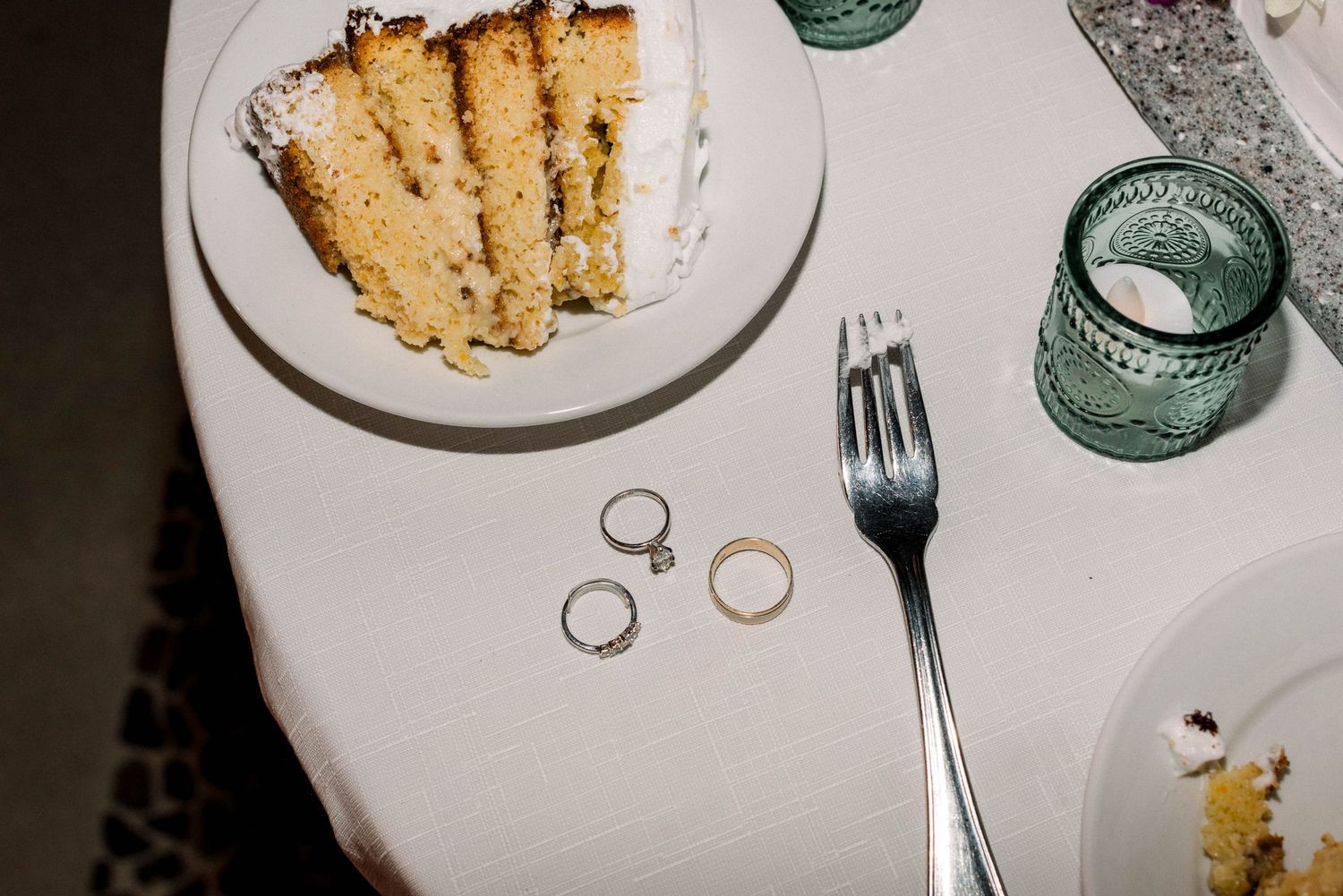 A slice of wedding cake on a plate with wedding rings displayed beside it.