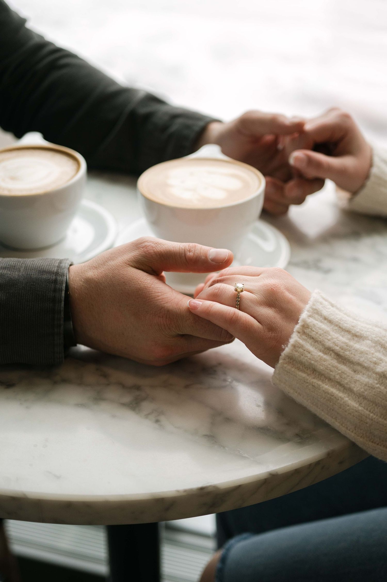 Two people hold hands across a marble table with coffee cups in a romantic moment.