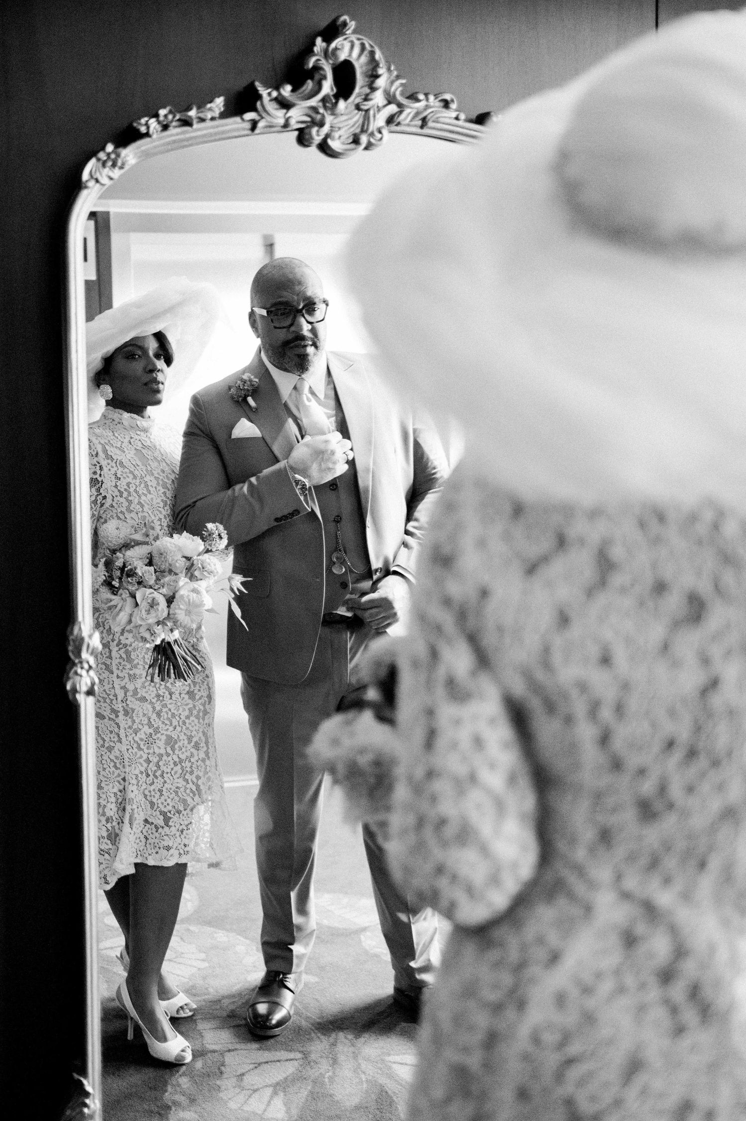 Black and white photo of wedding couple reflected in ornate mirror frame.