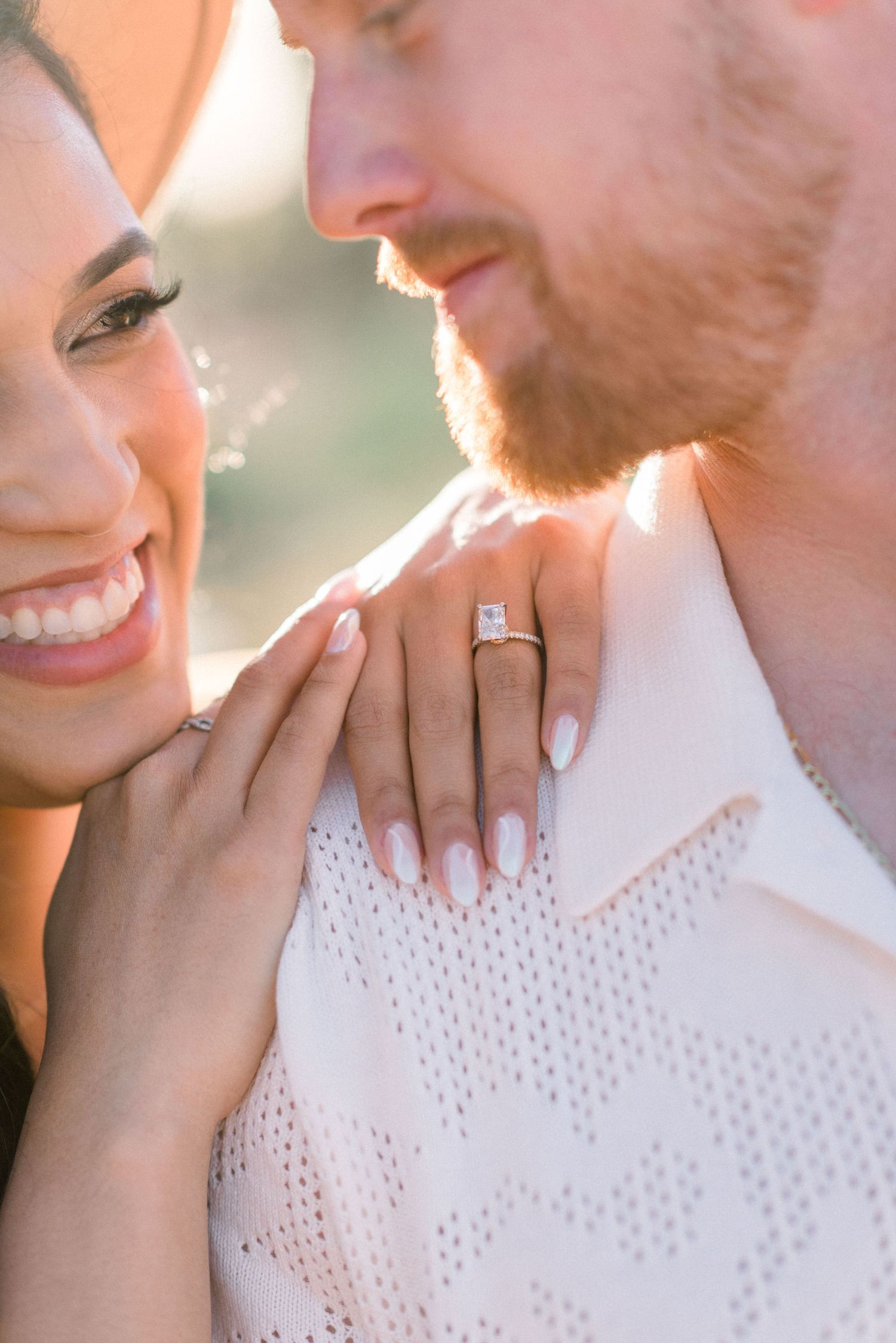 Close-up shot of couple showing engagement ring with woman's hand on man's white textured shirt.