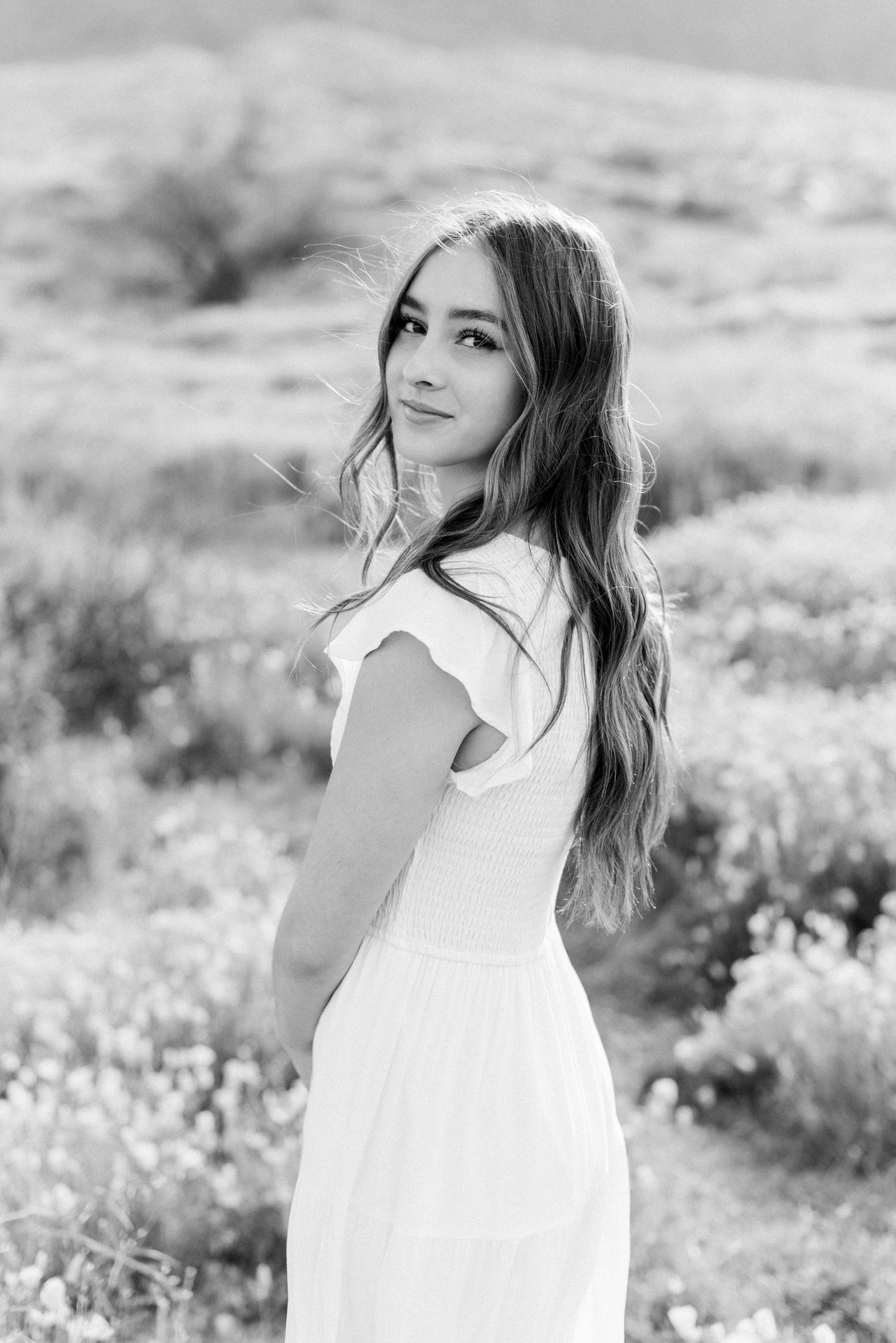 Black and white portrait in flowing white dress against natural landscape.