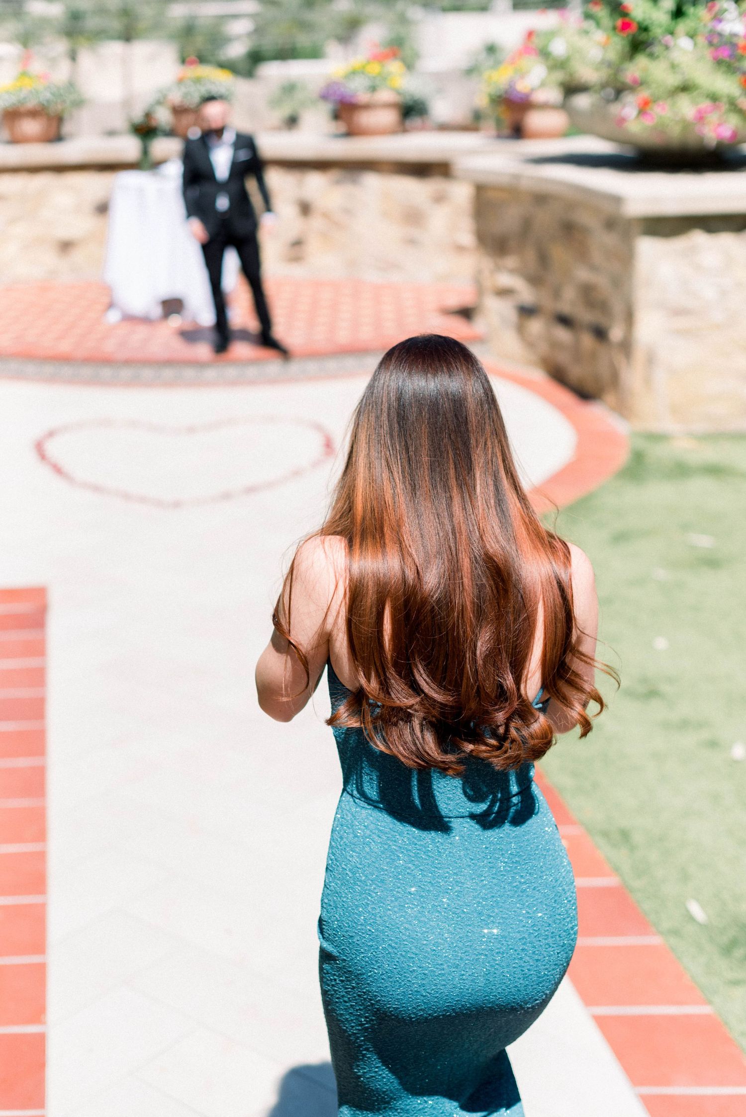 Figure in teal dress walks towards couple in distance during outdoor photoshoot.