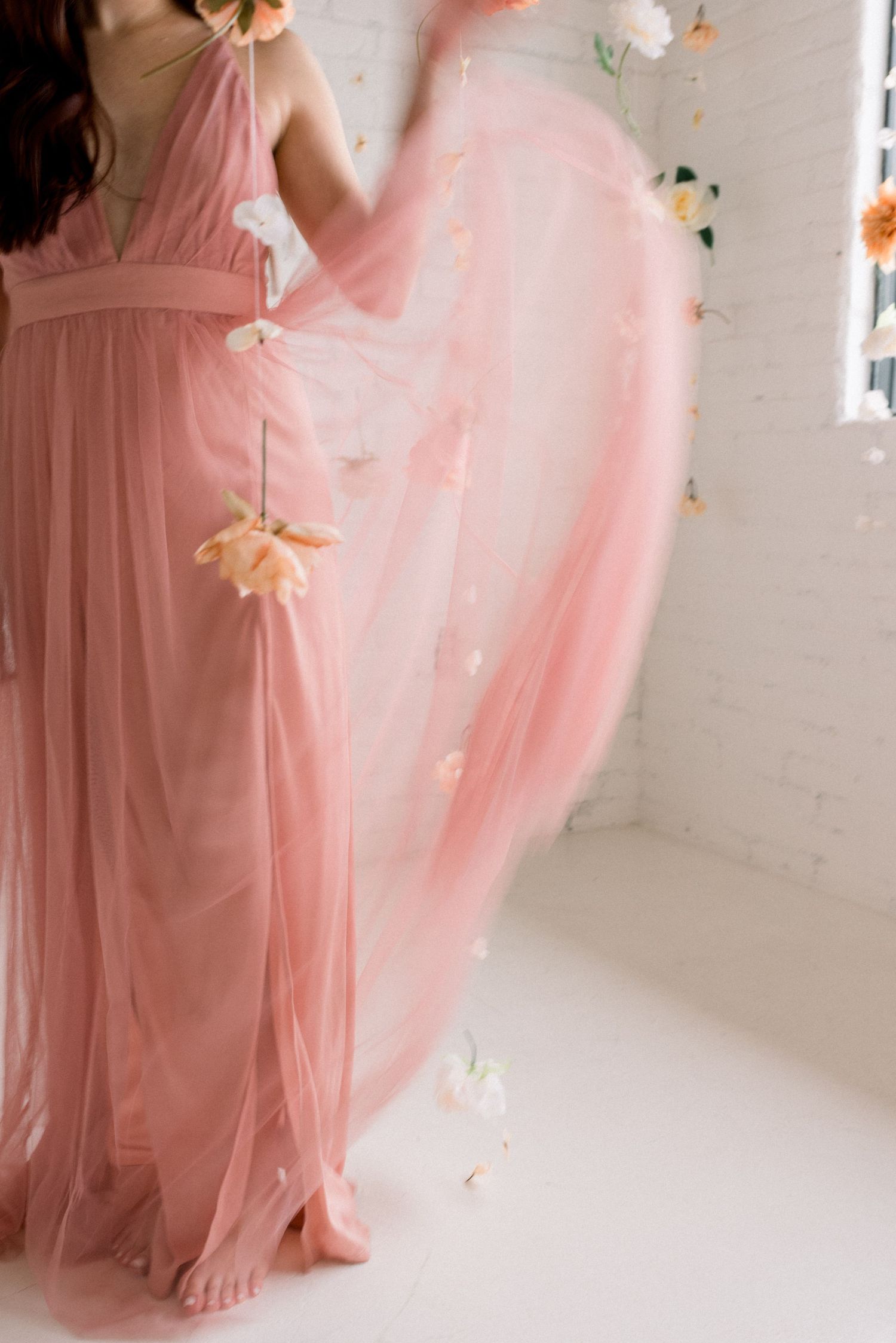 Ethereal pink dress with delicate tulle fabric swirling among suspended floral decorations.