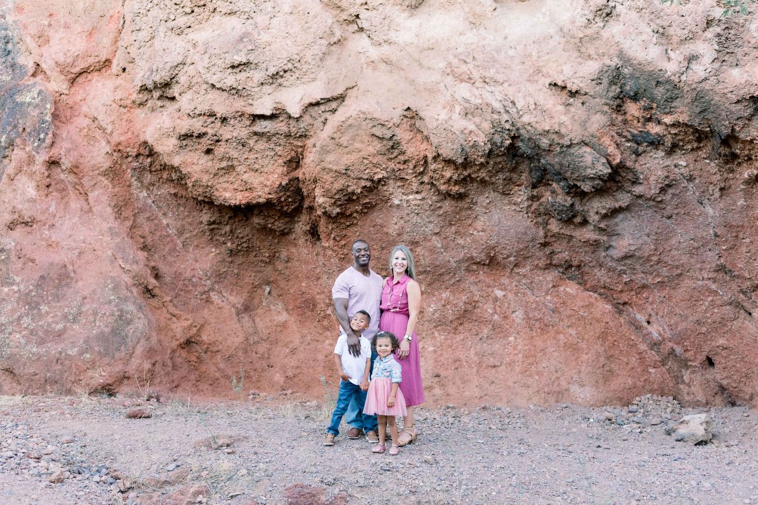 Family standing against pink rock formation in desert landscape.
