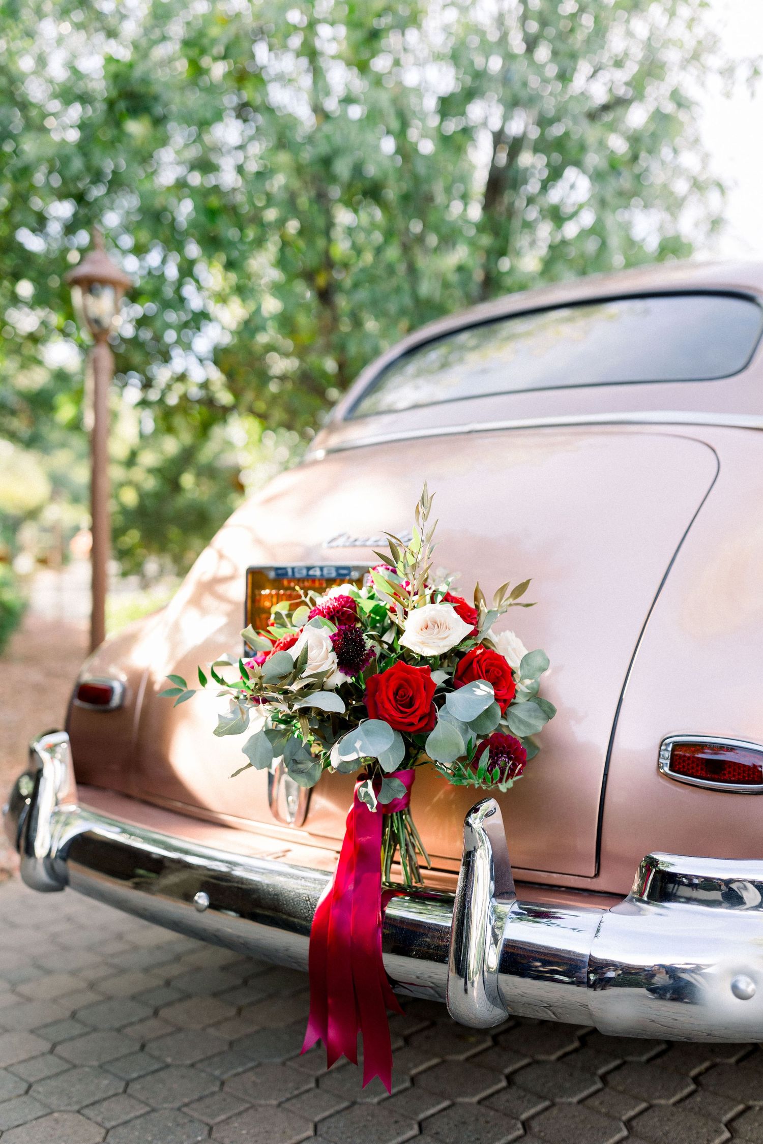 Vintage pink Chevrolet adorned with red and white wedding bouquet and burgundy ribbons.