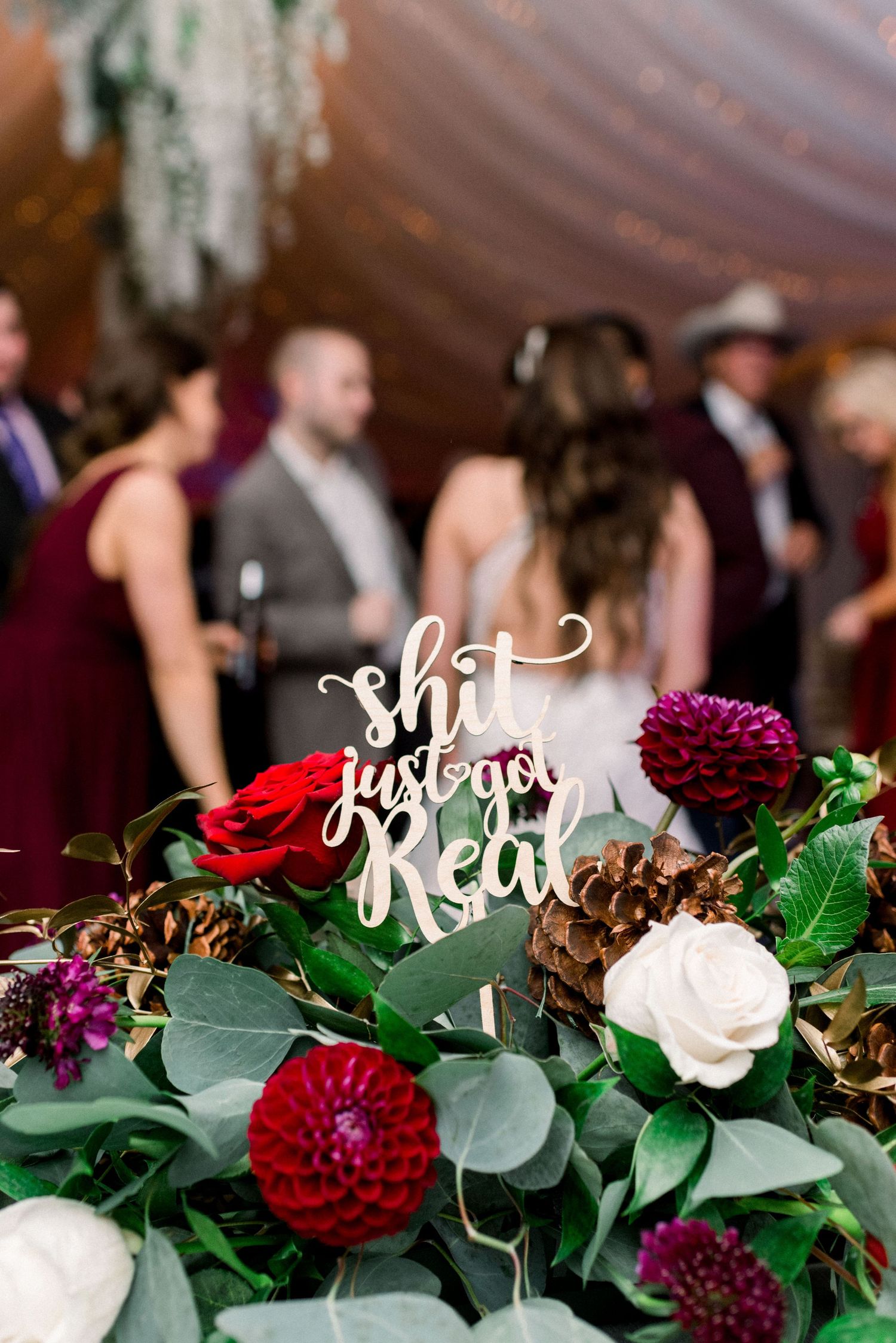 Floral centerpiece with red and purple dahlias featuring decorative text at wedding reception.