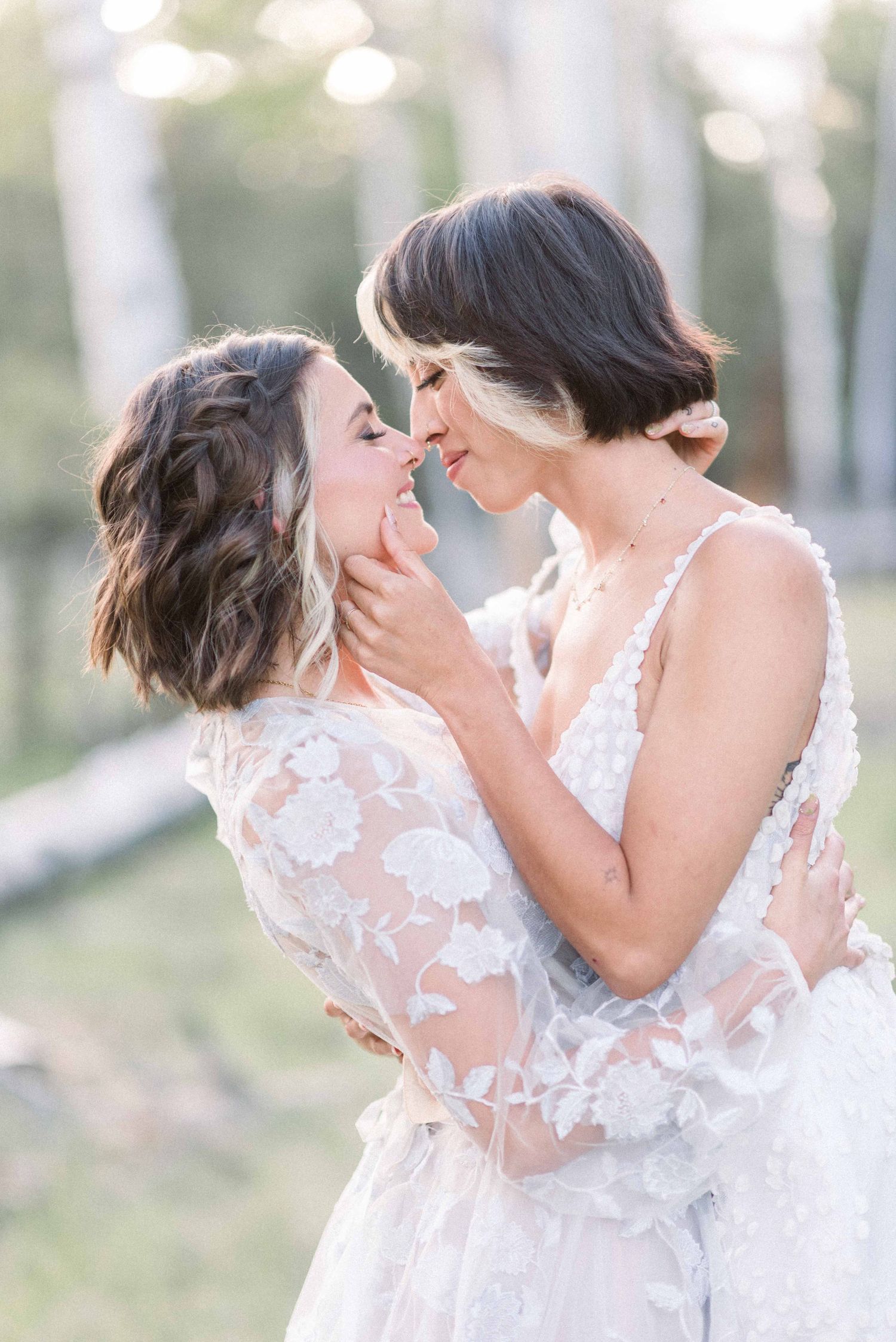 Intimate moment between newlyweds wearing white lace dresses in outdoor setting.