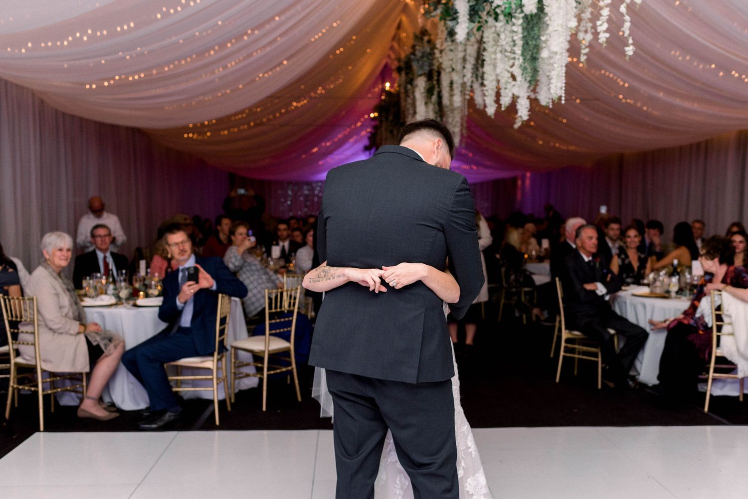 Couple embracing during first dance with wedding guests watching from their tables.