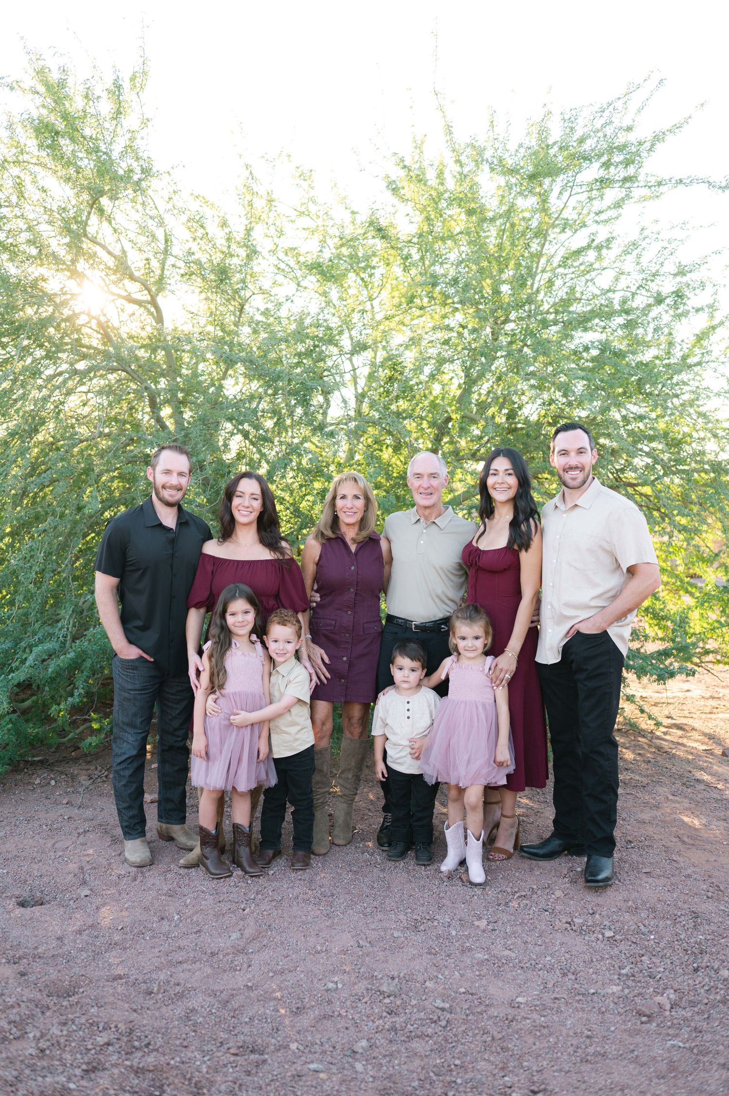 Family group poses outdoors in coordinated burgundy and pink outfits against desert landscape.