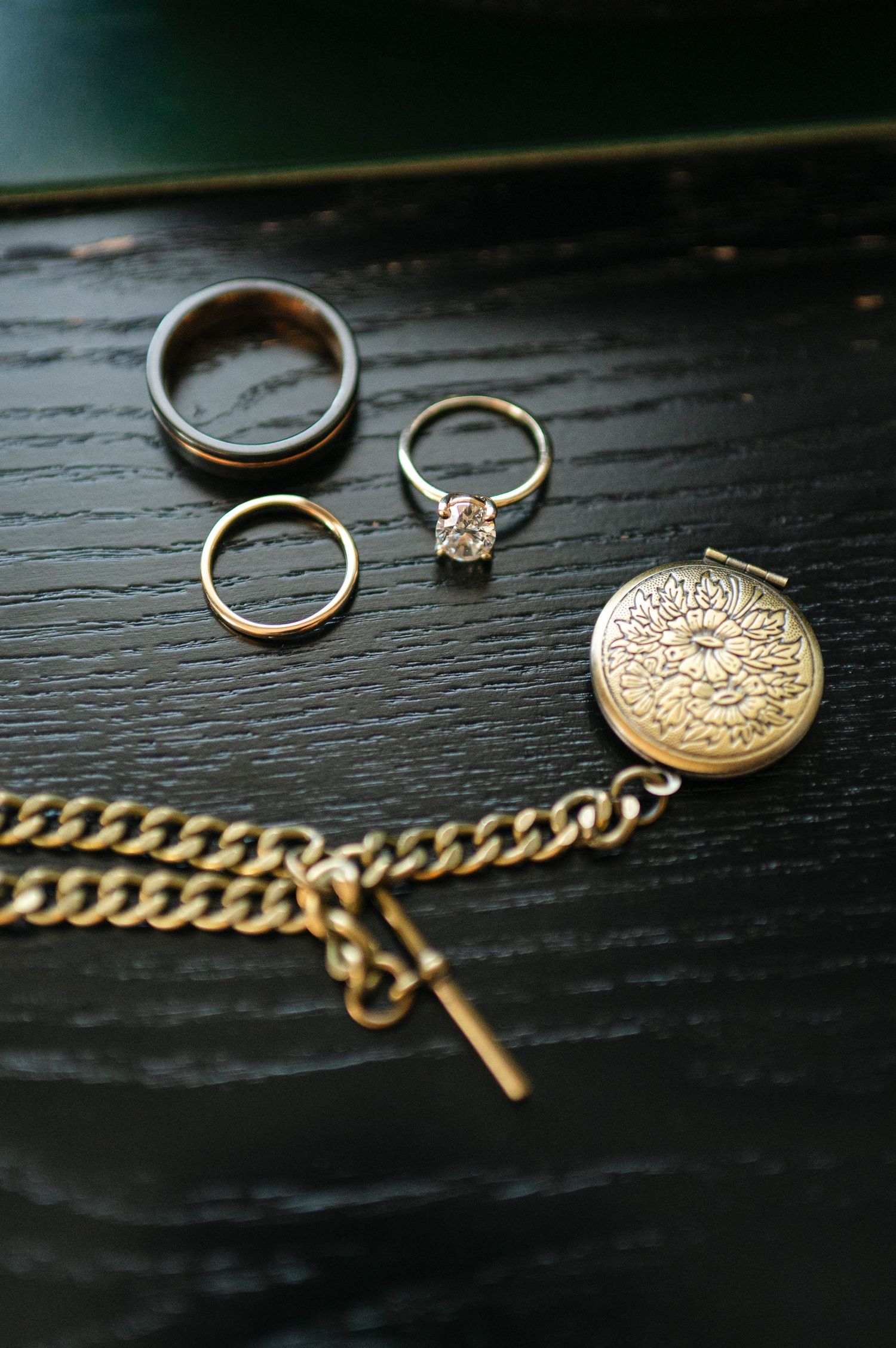 Gold jewelry pieces including rings, chains, and lockets arranged on dark wooden surface in vintage style composition.